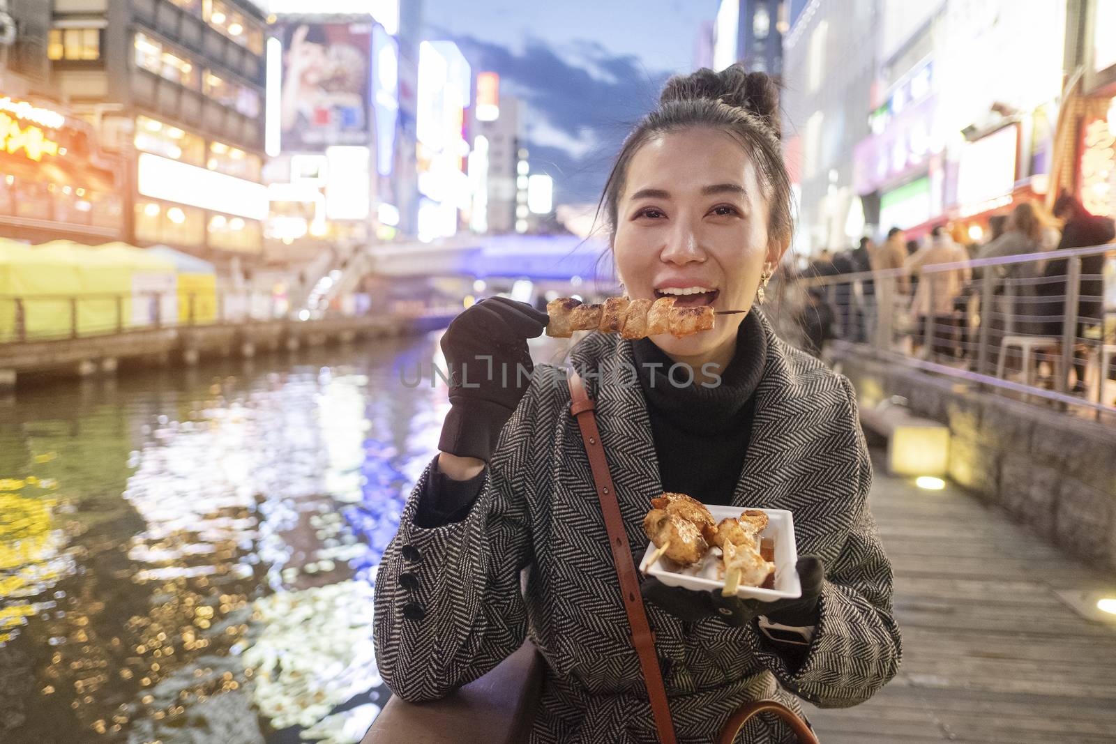 Young woman tourists enjoy eating street food in walking at street shopping center Dotonbori in Osaka, Japan.