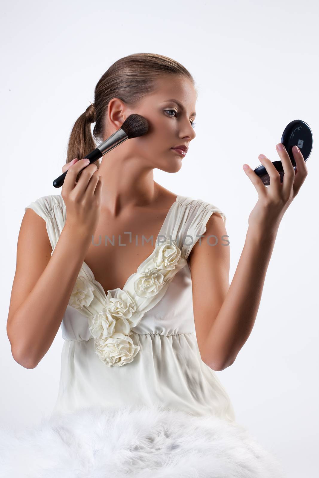 Young beautiful woman applying cosmetics onto her face