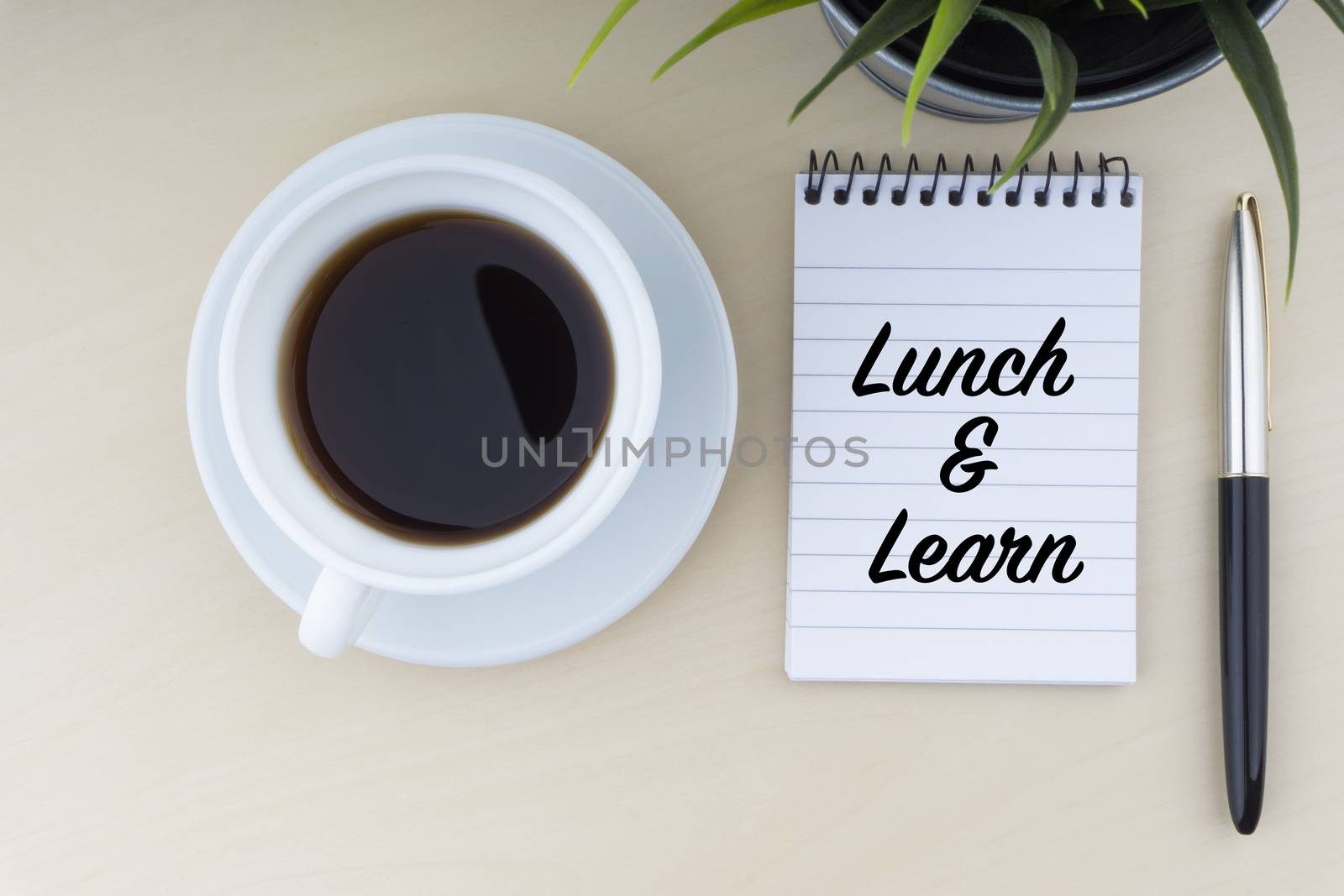 LUNCH AND LEARN text with fountain pen, notepad, and decorative flower on wooden background by silverwings