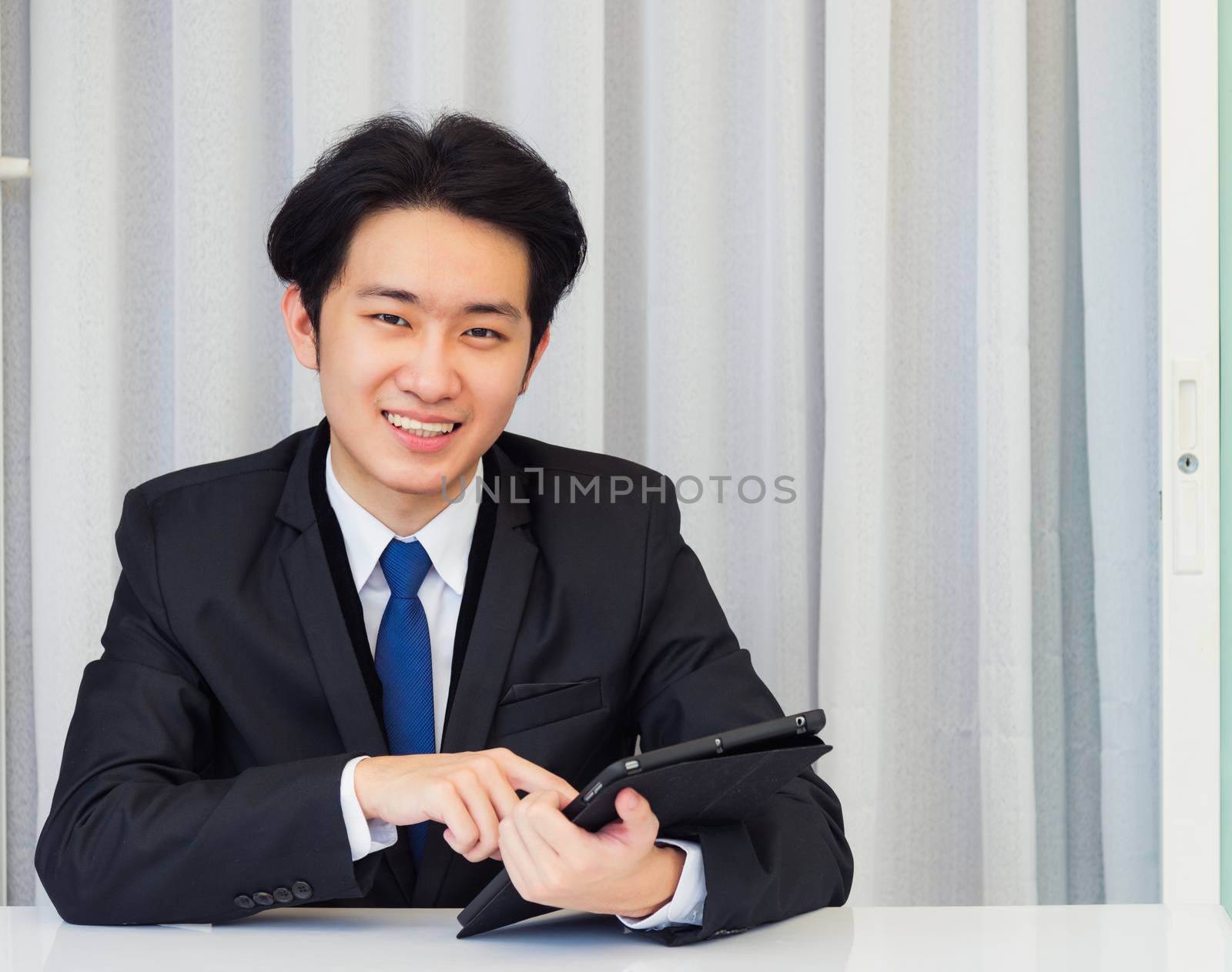 Work from home, Asian young businessman video conference call or facetime he smiling looking to camera sitting on desk using smart digital tablet computer touching on screen at home office
