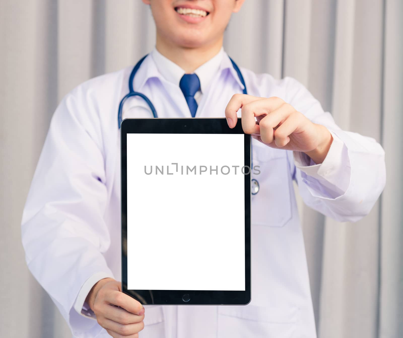 Portrait closeup of Happy Asian young doctor handsome man smiling in uniform and stethoscope neck strap showing front blank screen smart digital tablet on hand, Healthcare medicine concept