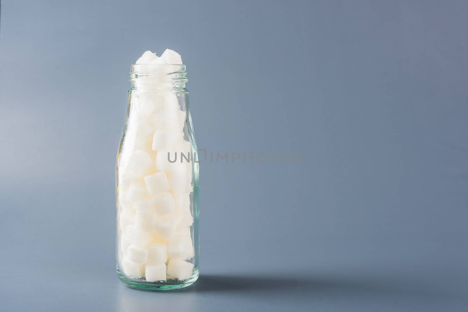Glass bottle full of white sugar cube sweet food ingredient, studio shot isolated on gray background, health high blood risk of diabetes and calorie intake concept and unhealthy drink