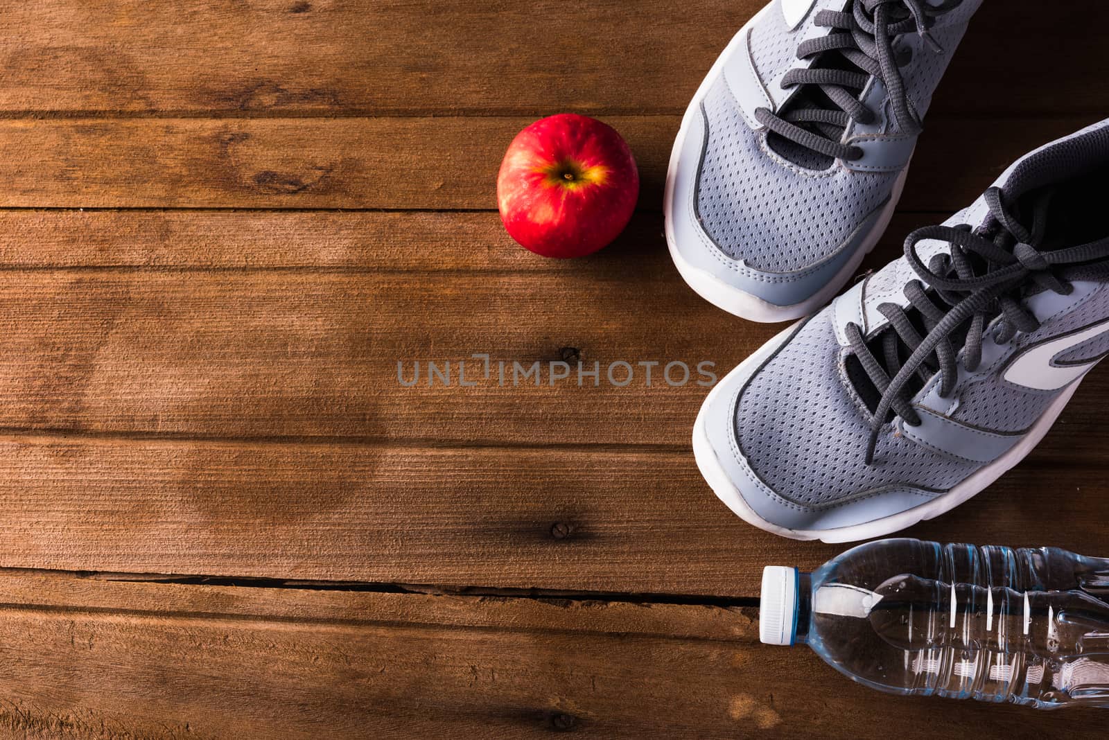 Top view of pair sports shoes, bottle water and red apple on wood table, Gray sneakers and accessories equipment in fitness GYM, Healthy workout concept