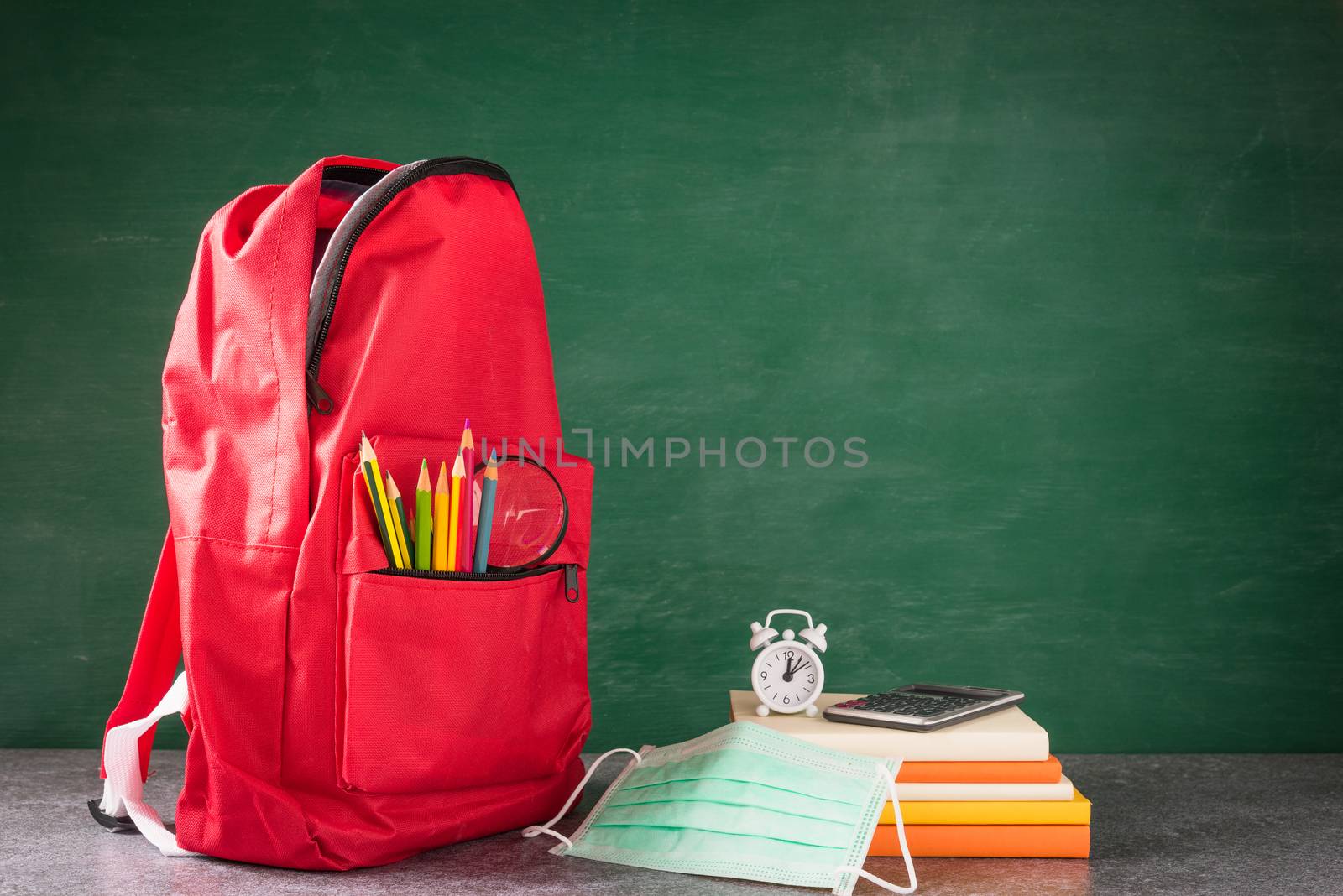 Front school backpack and accessories with face mask protect on desk at green chalkboard, student bag at classroom backboard, Back to school education new normal outbreak COVID-19 or coronavirus