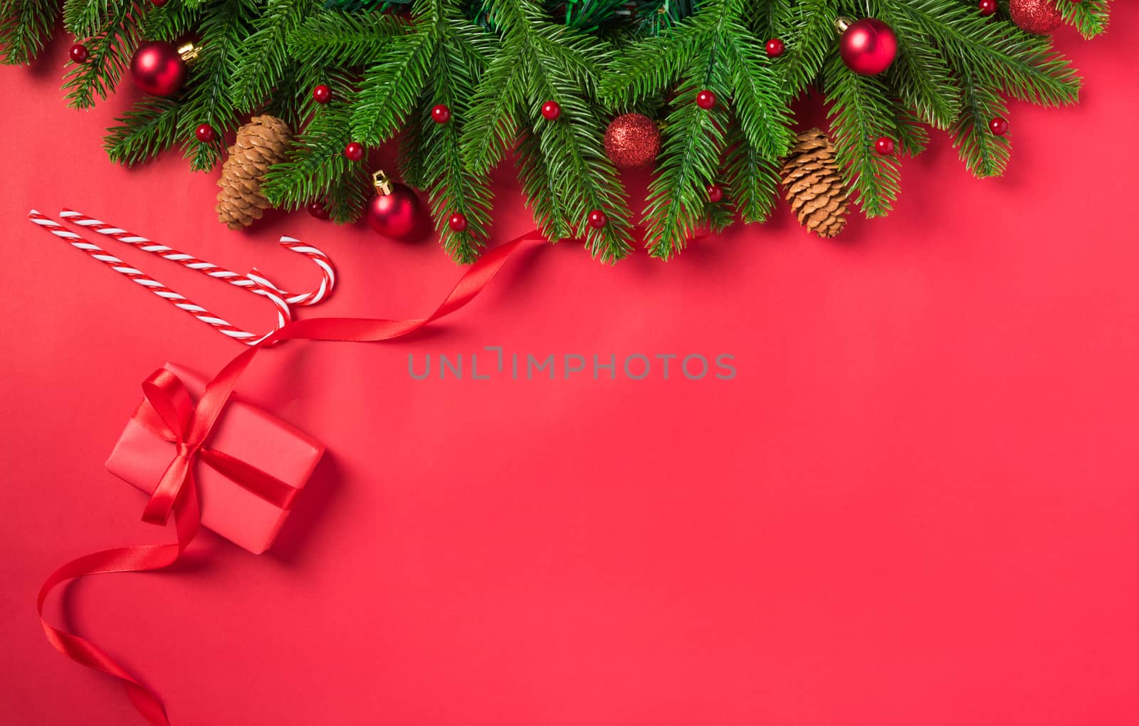 Christmas holiday background with gift box decorations composition, Top view fir green fir tree branches and Xmas ornaments on a red table background