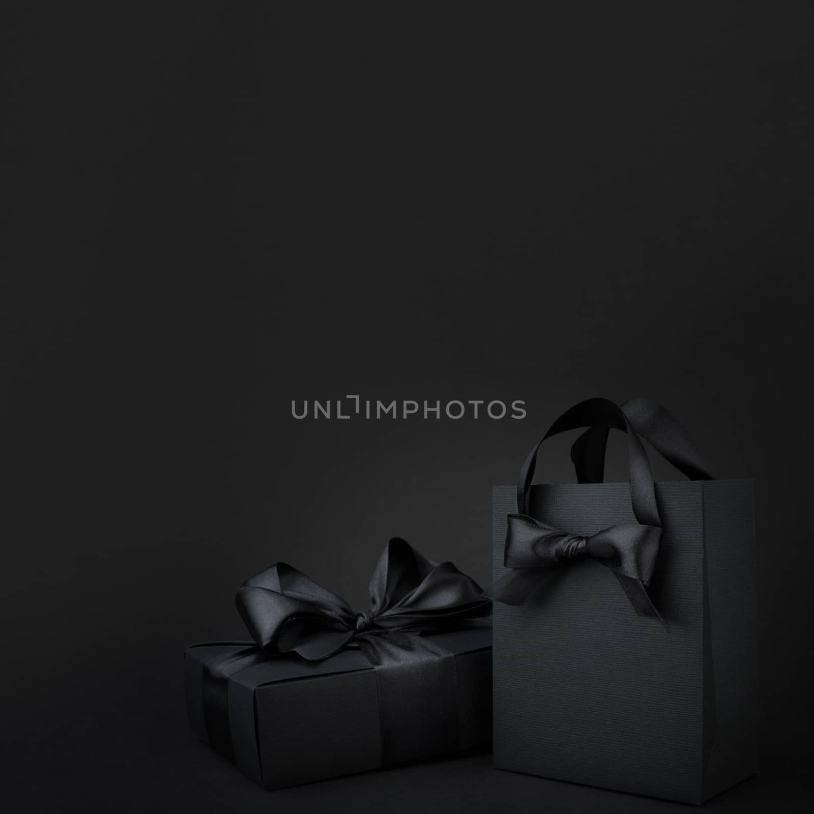 Concept sales, shopping, black friday. Paper shopping or gift bag box with silk ribbon bow on black background with copy space