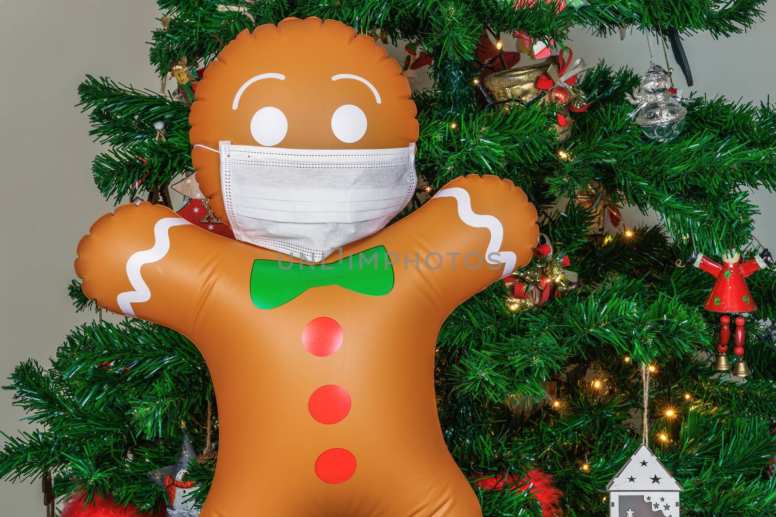 Air blown seasonal gingerbread figure before illuminated artificial decorated green tree with lights.