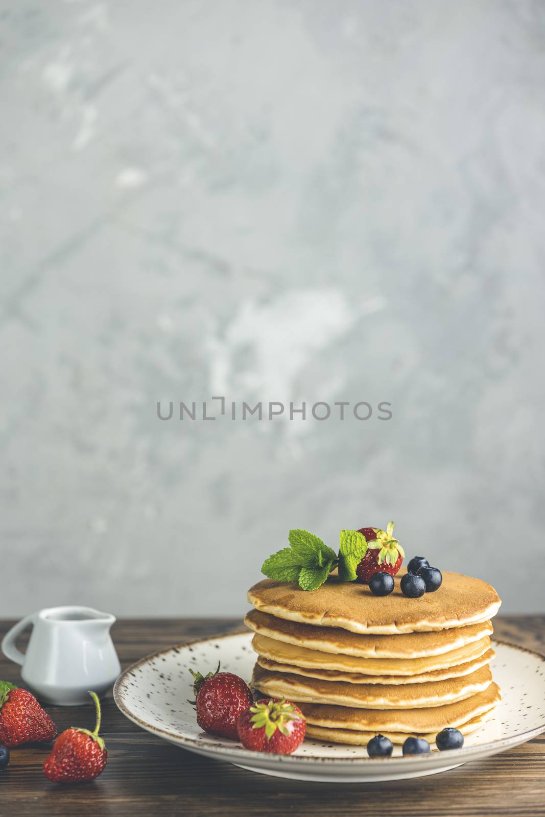 Pancake with strawberry, blueberry and mint in ceramic dish, syrup from small ceramic jar
