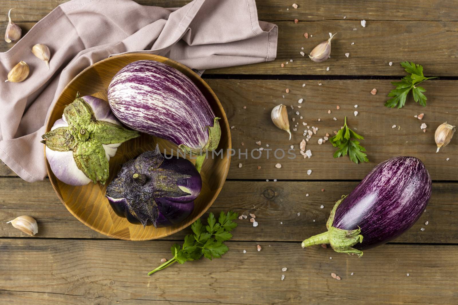 Wooden pot with different raw fresh eggplant. Dark wooden background. Concept of green house life style and products of subsistence farming, flat lay, copy space