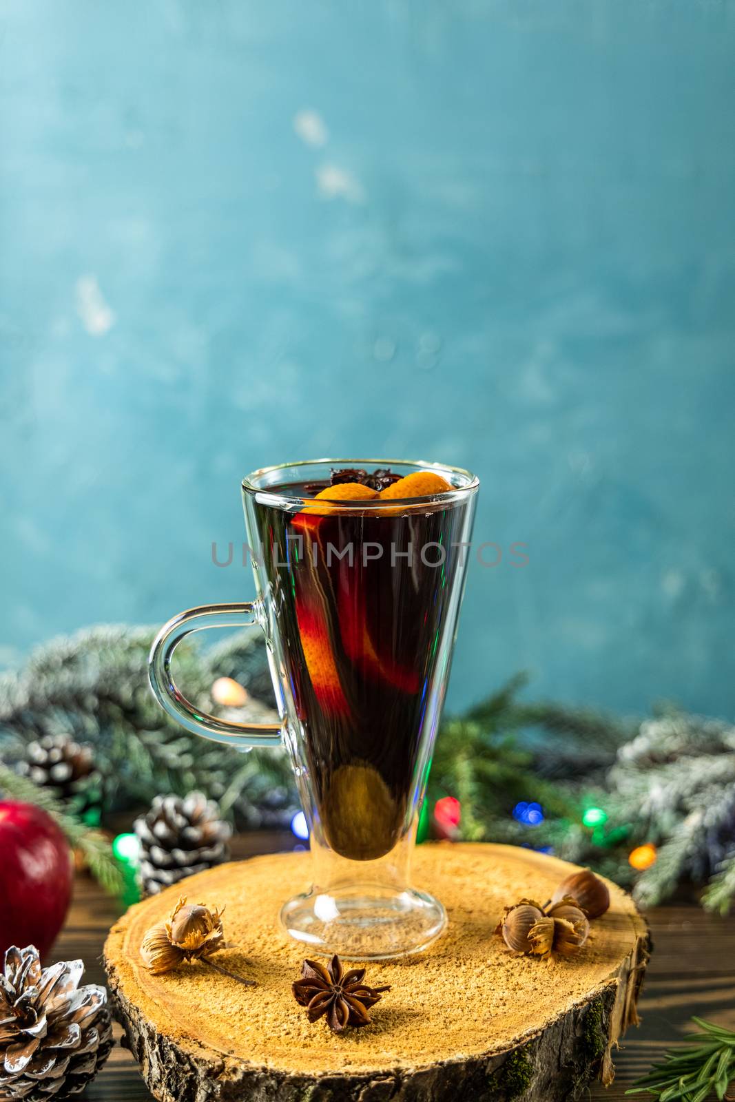 Hot mulled wine drink with orange, apple, cinnamon, anise and other spices in a glass cup between fir tree branches on wooden cutting board