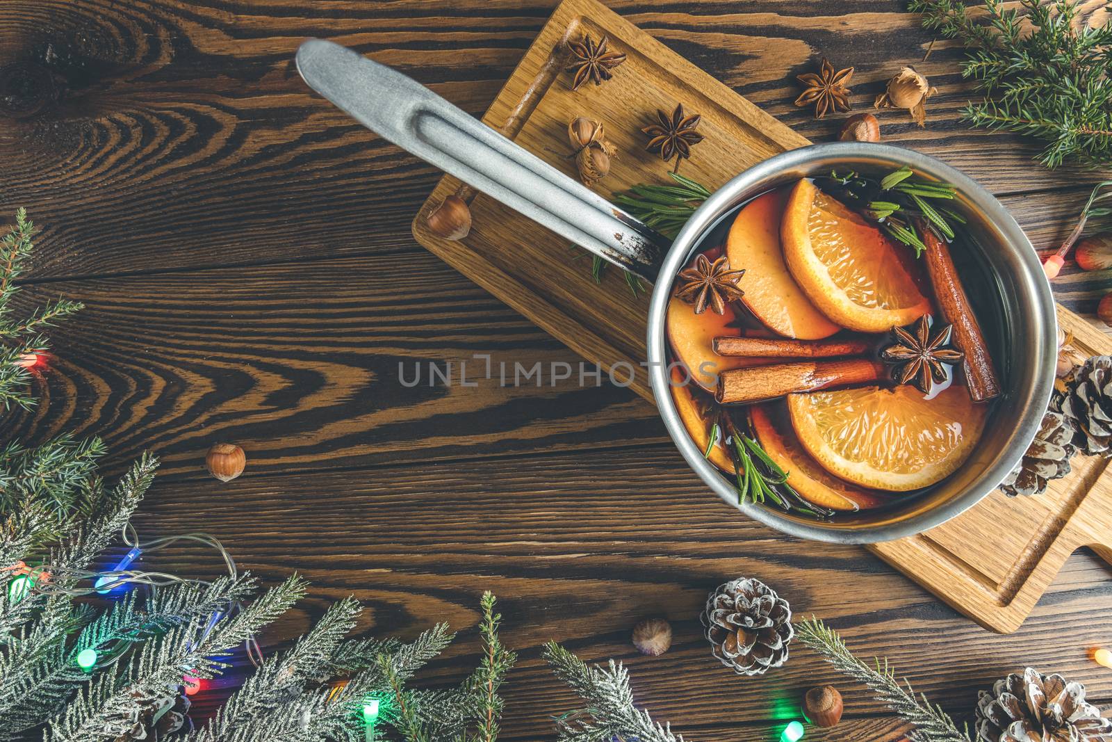 Christmas mulled red wine with the addition of spices and citrus fruits in a small metal pan on a rustic wooden table, top view. Pot of mulled wine, traditional christmas drink.