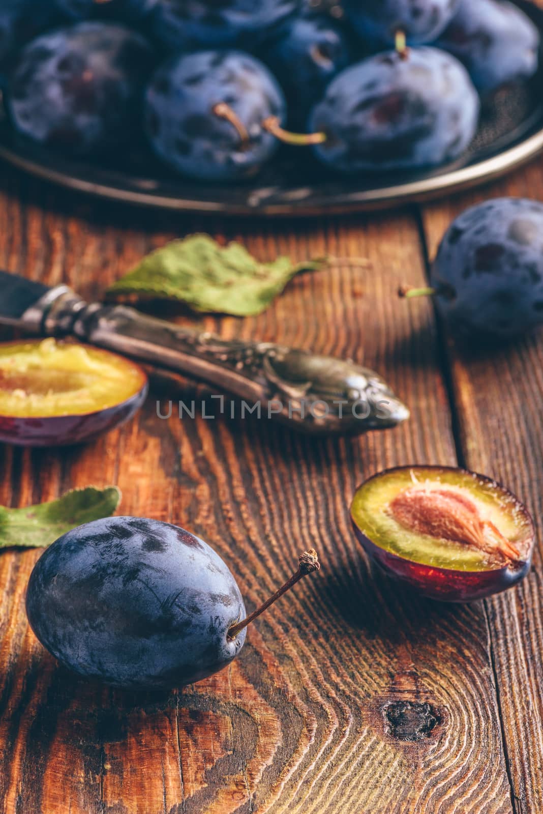 Ripe plums on metal tray and dark wooden surface with leaves and vintage knife