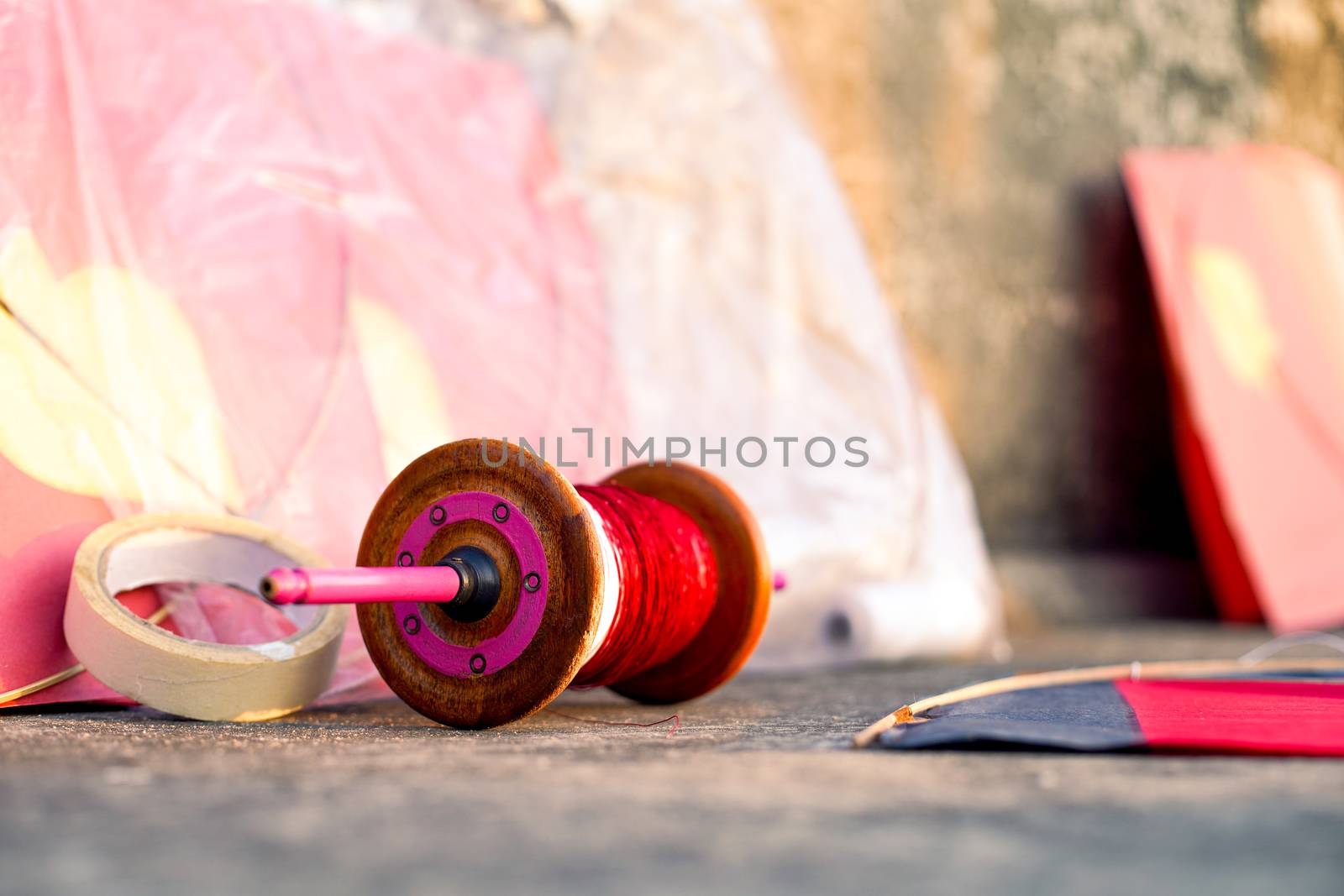 series of colorful red yellow paper and wood kits placed near fikri charki spools filled with dor plain thread and manjha glass covered thread for the indian festival of makar sankranti uttarayana by Shalinimathur