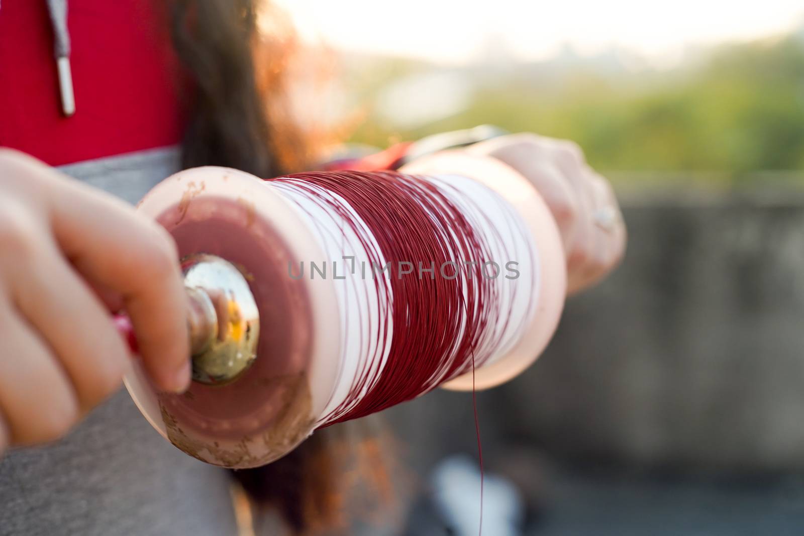 Man holding a charki phirki thread spool in the crook of his elbow and winding it with the other hand to ensure taughtness for the famed kite fighting festival of makar sankranti uttarayana by Shalinimathur