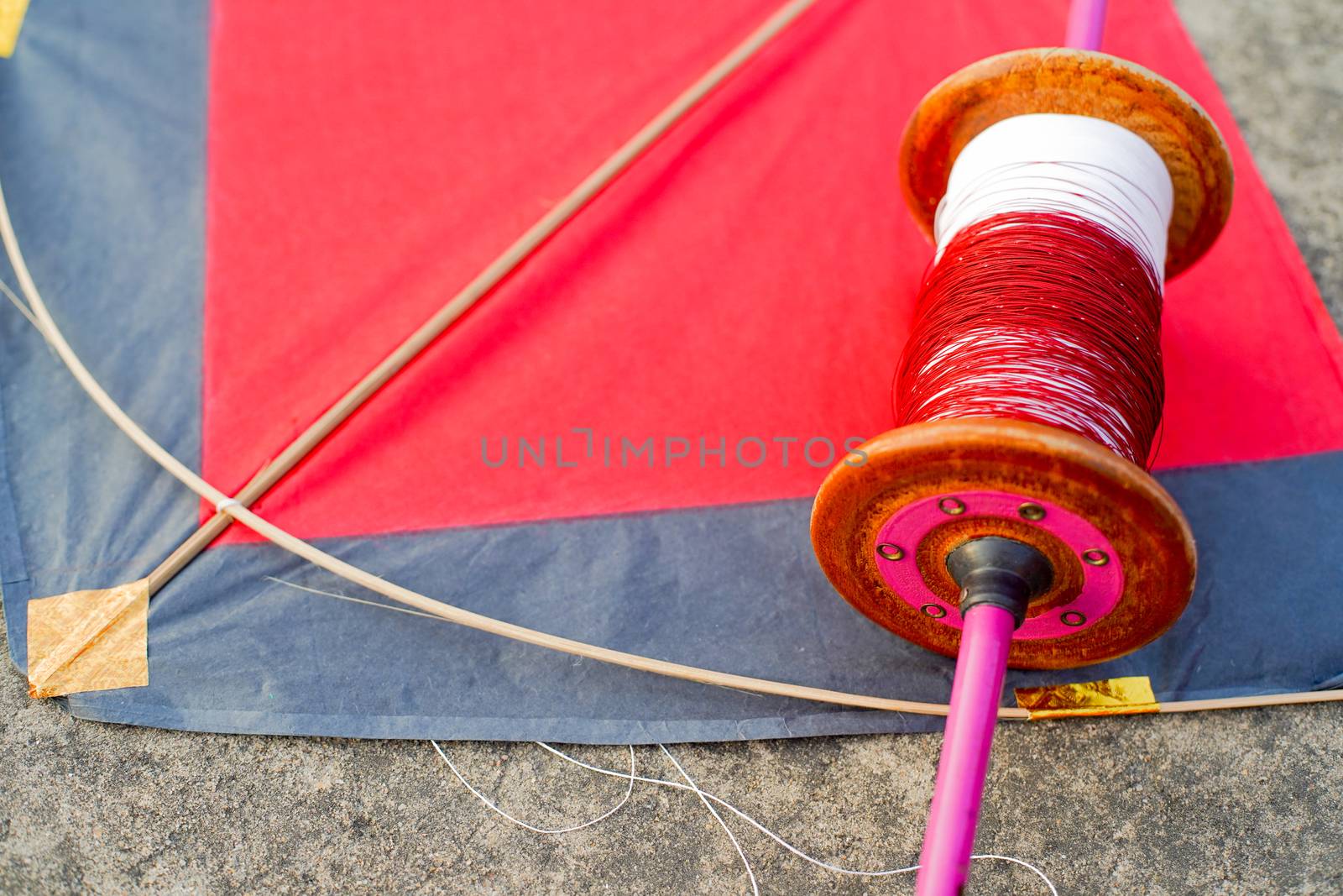 Top down flatlay shot with red and black paper and wood kite with a wooden handmade charkhi thread spool with normal and glass covered thread for kite fighting on teh indian festival of makar sankranti uttarayana . This festival is known for its colorful kites of paper and wood used for kite fighting with a glass covered thread to cut an opponents kite