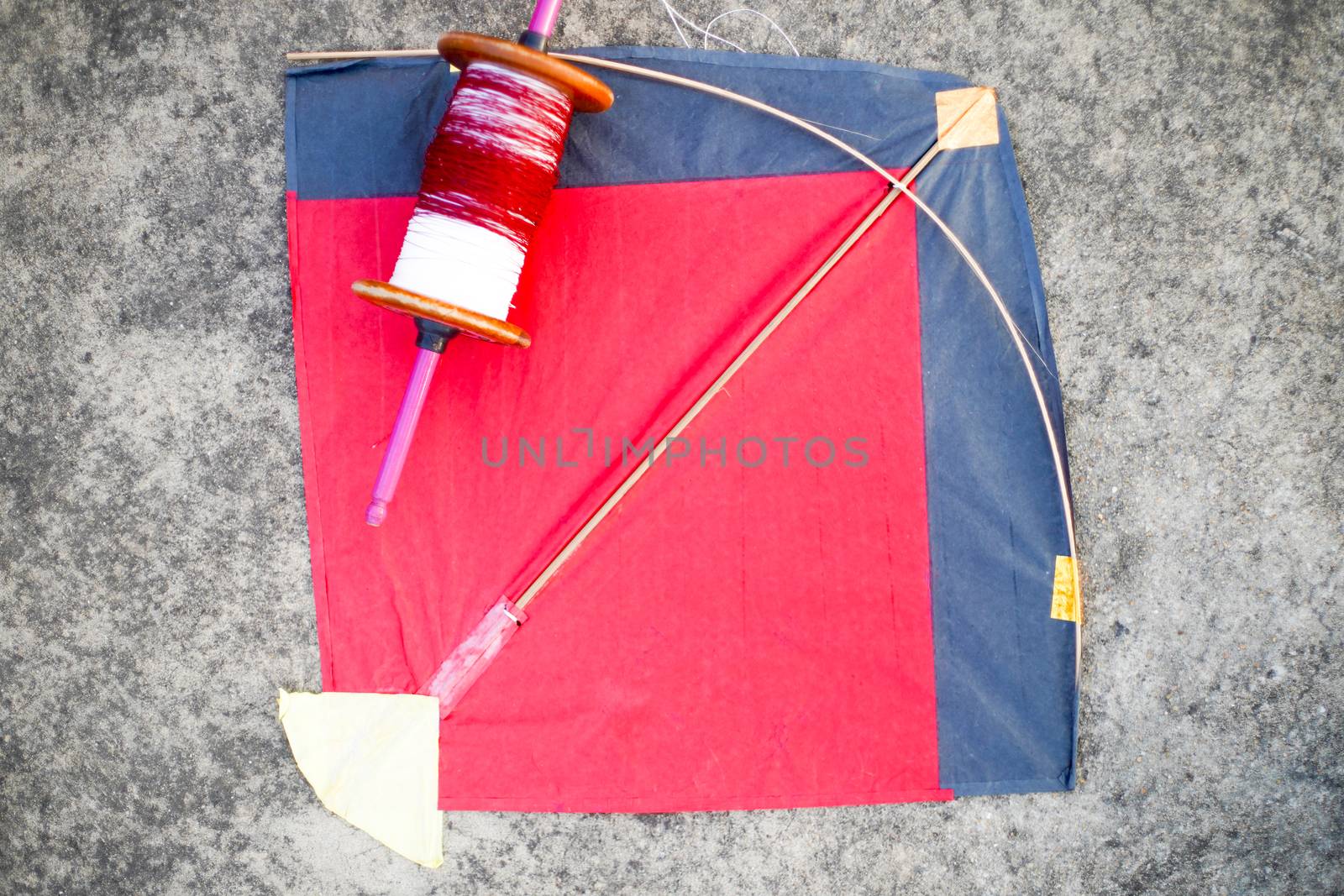 Top down flatlay shot with red and black paper and wood kite with a wooden handmade charkhi thread spool with normal and glass covered thread for kite fighting on teh indian festival of makar sankranti uttarayana . This festival is known for its colorful kites of paper and wood used for kite fighting with a glass covered thread to cut an opponents kite