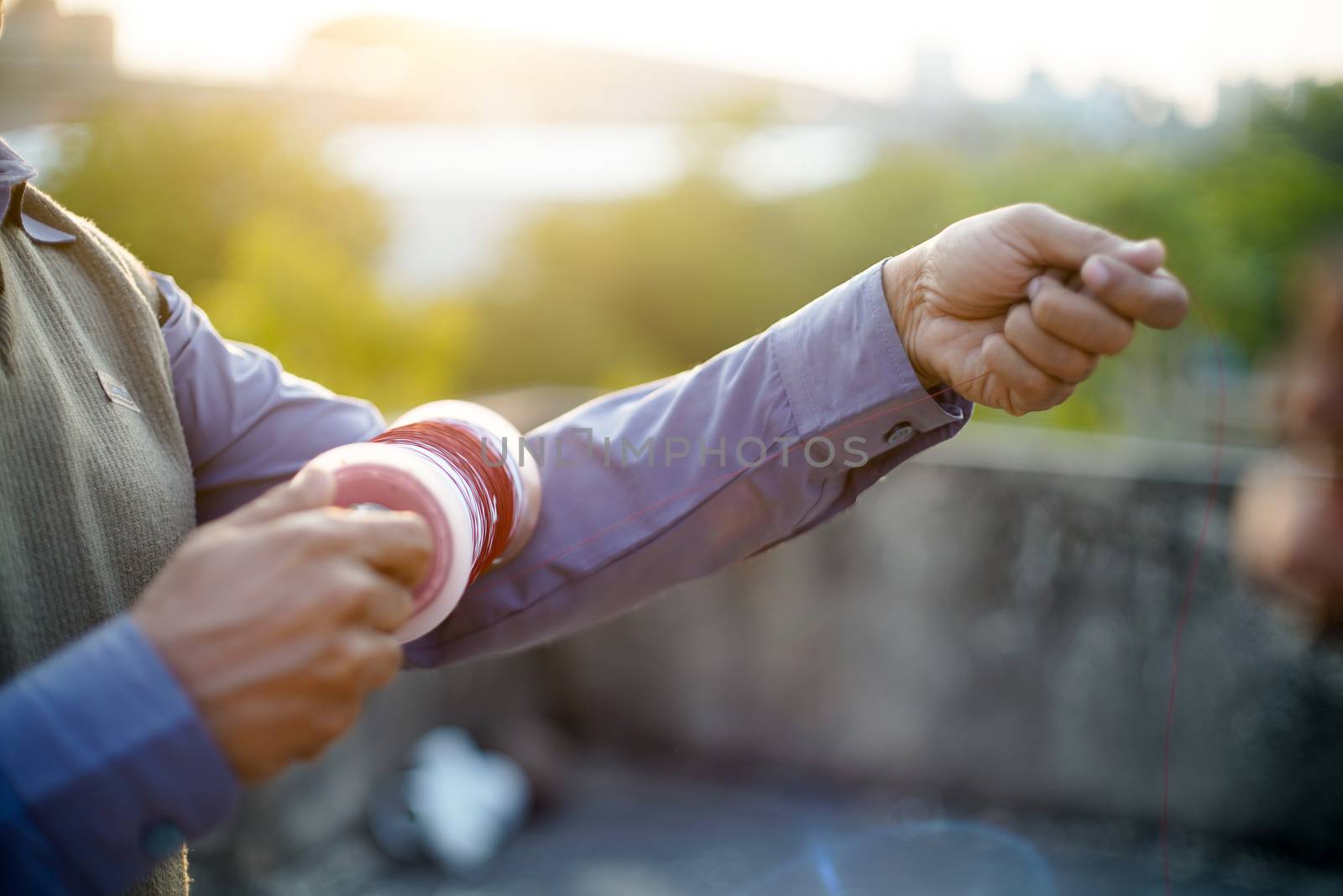 Man holding a charki phirki thread spool in the crook of his elbow and winding it with the other hand to ensure taughtness for the famed kite fighting festival of makar sankranti uttarayana by Shalinimathur