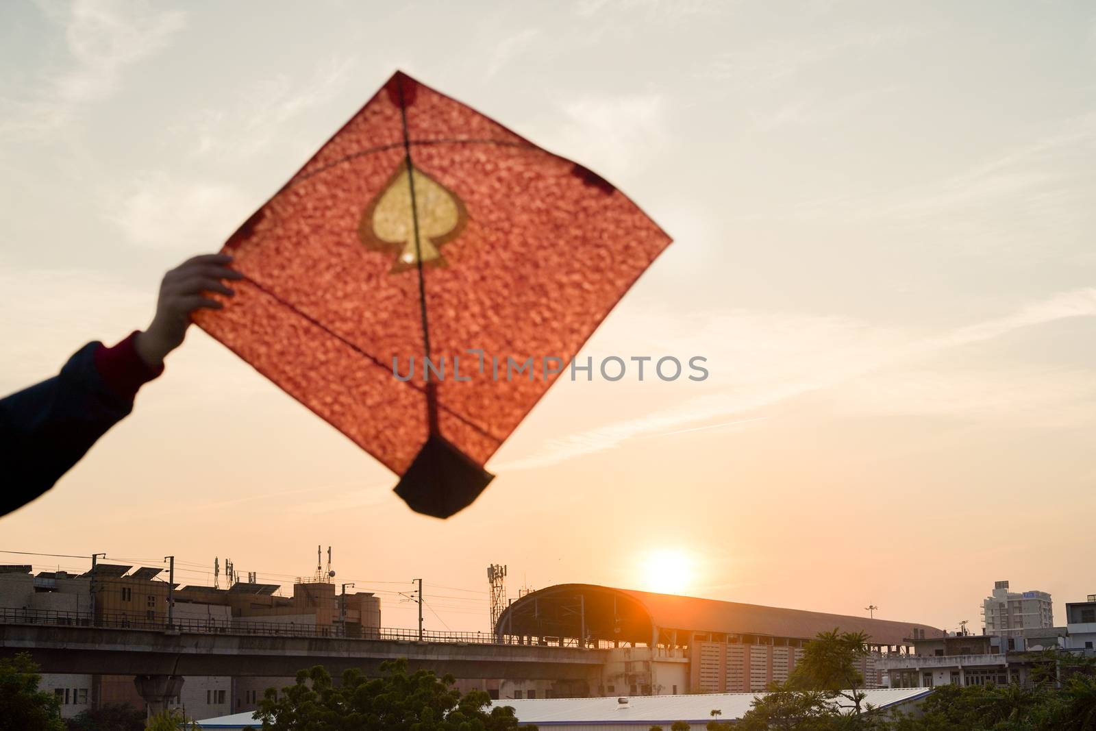 Young man holding aloft colorful paper and wood kite against a blurred background setting sun on the indian kite festival of makar sankranti or uttarayana. This festival is known for its colorful kites of paper and wood used for kite fighting with a glass covered thread to cut an opponents kite