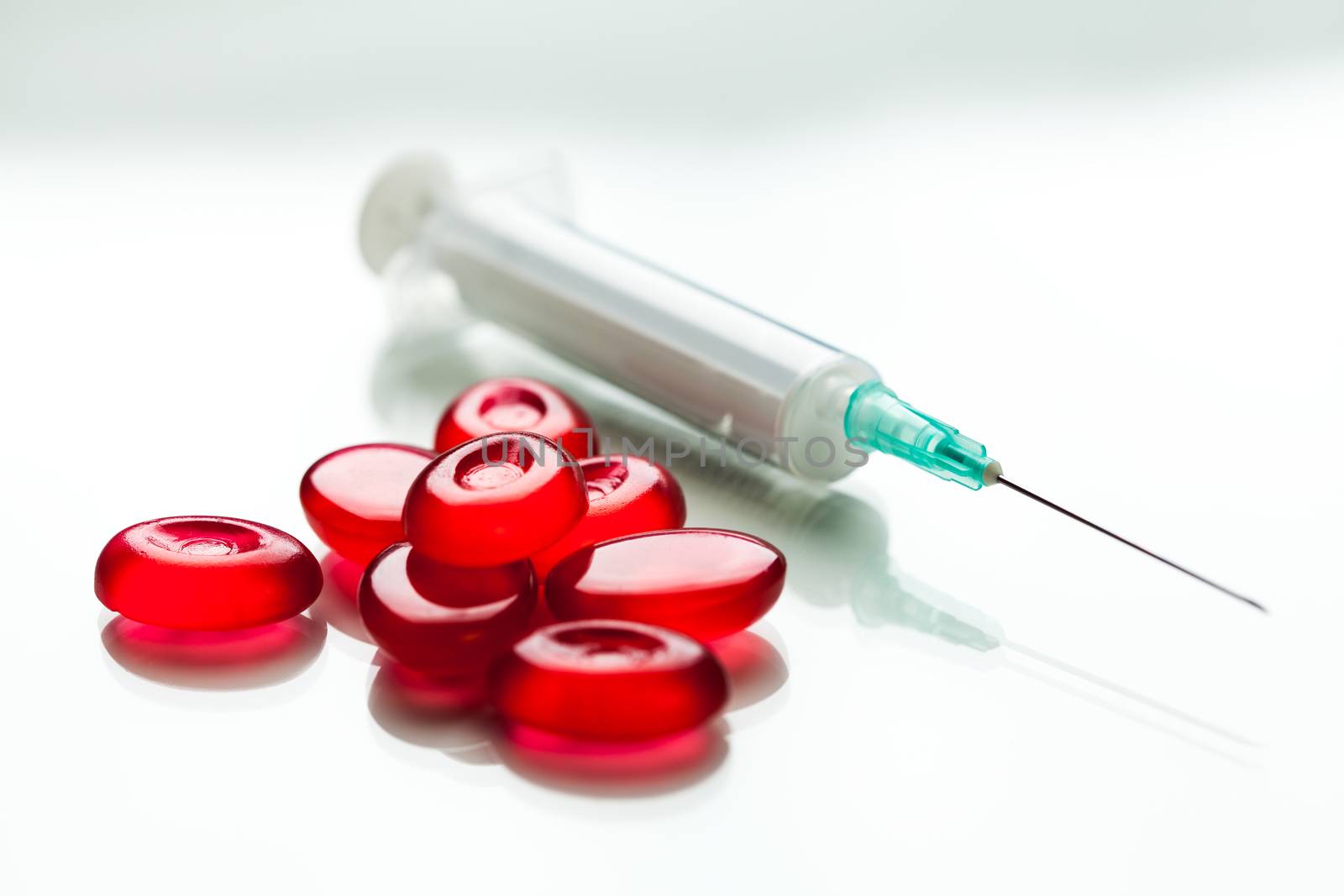 Pile of red pills & syringe with needle by Plyushkin