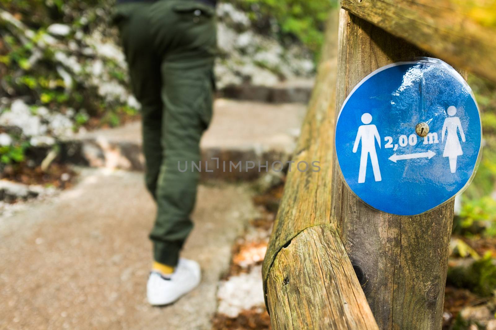 Blue round sign on a wooden fence informing people to keep 2 meter social distance by Plyushkin