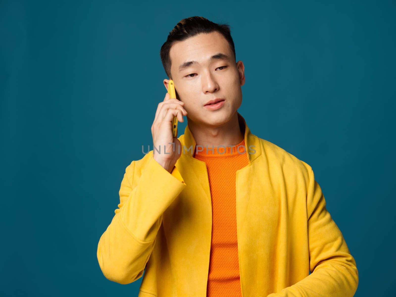 A handsome Korean man in a yellow jacket on a blue background with a phone in his hands. High quality photo