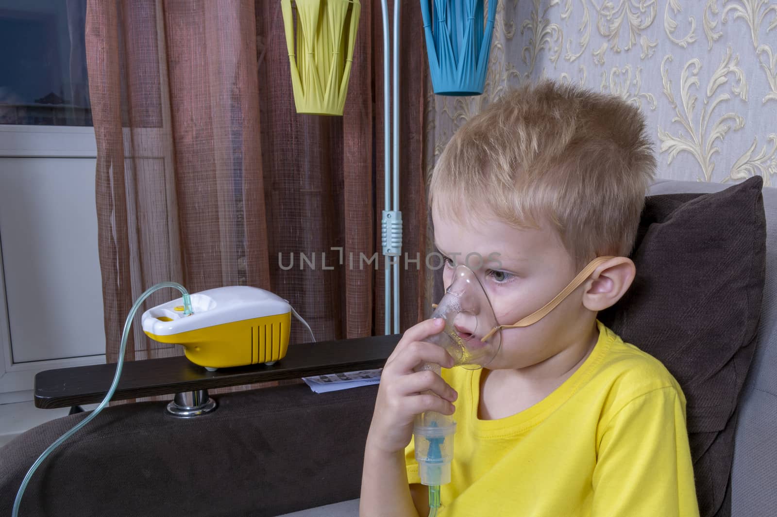a 5-7 year old boy in a yellow t-shirt takes an inhalation at home by Akmenra