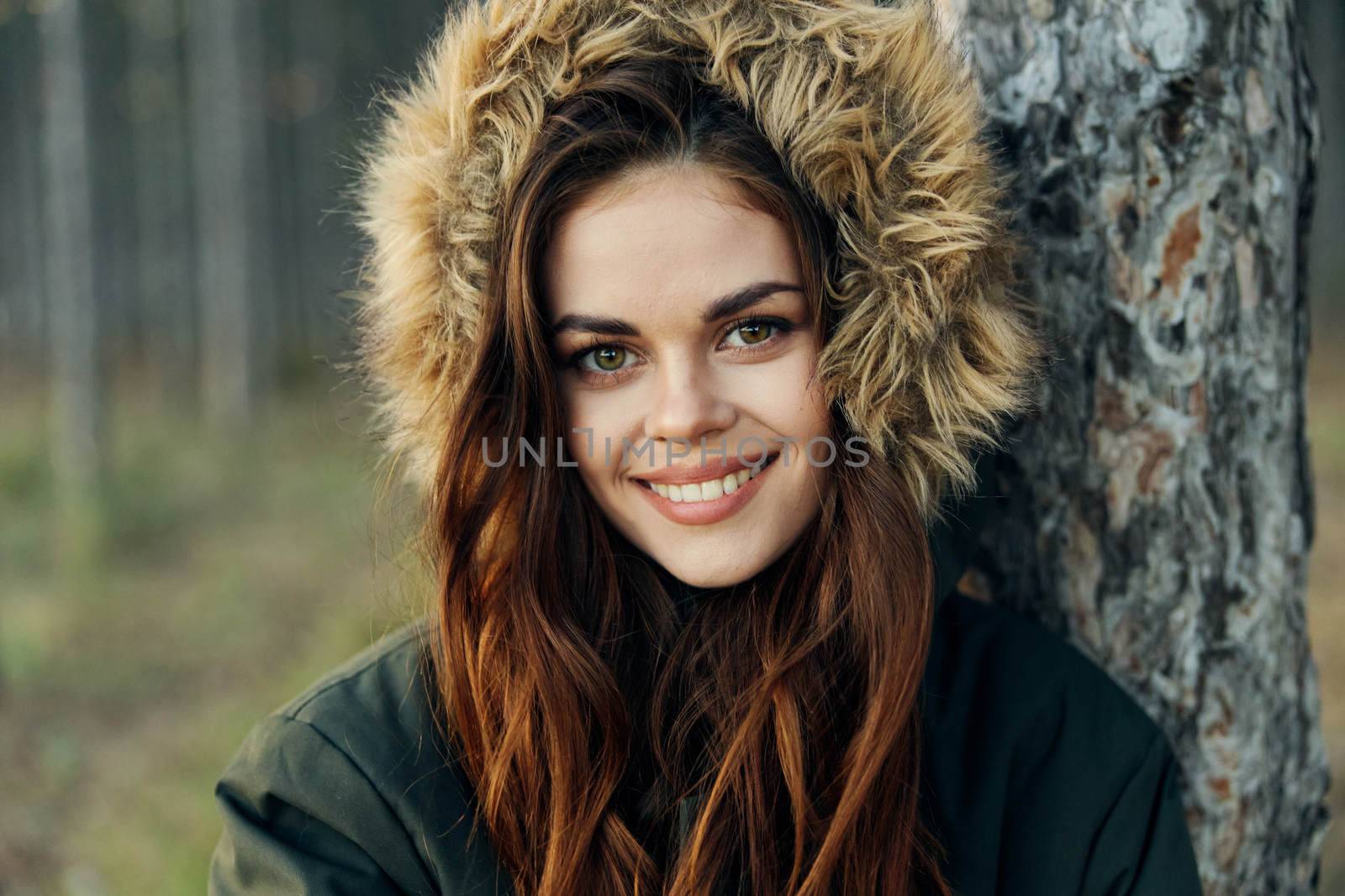 Woman in a jacket with a hood near a tree on a forest background cropped view. High quality photo