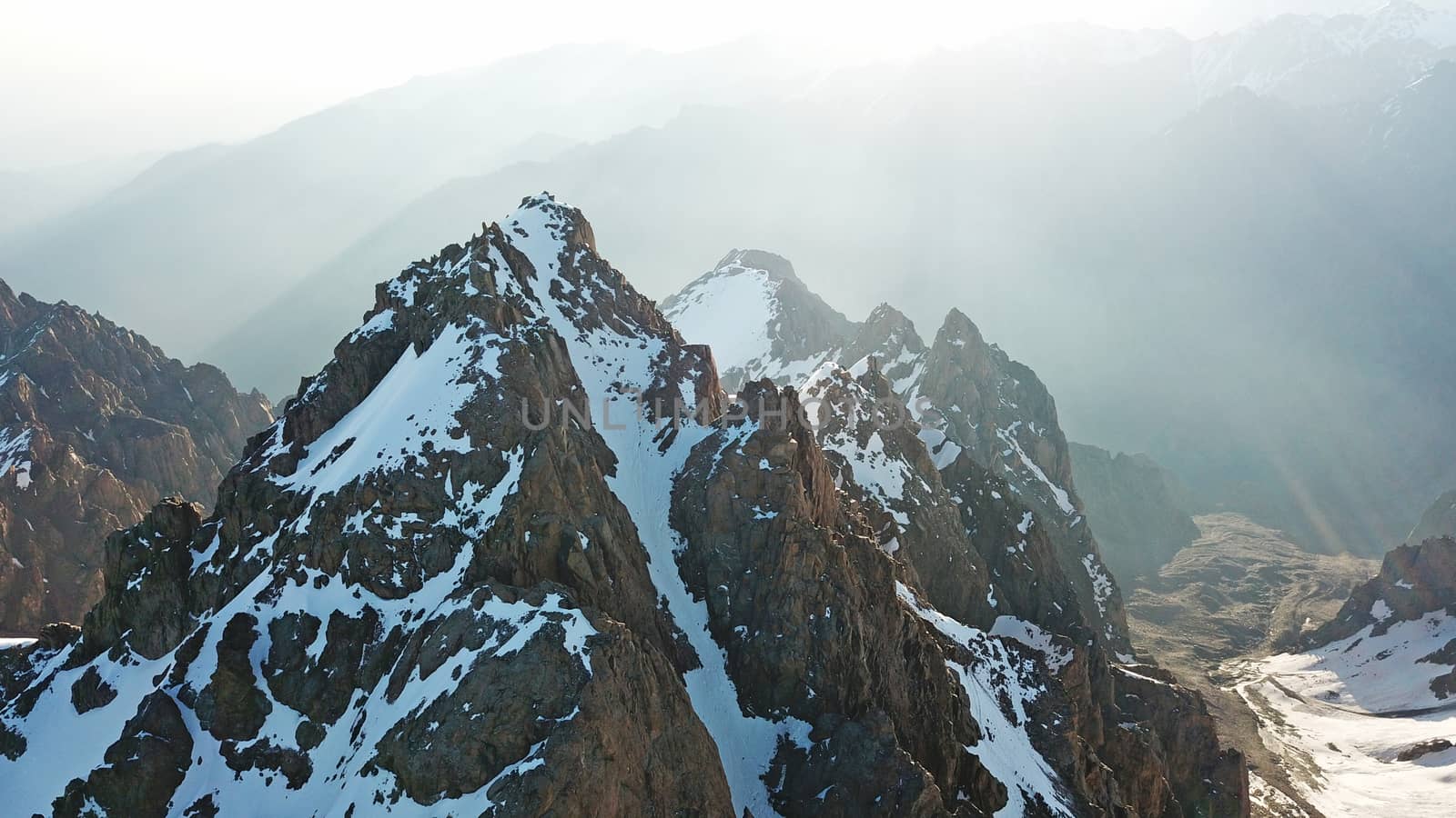 Huge snow mountains. View from the top of the drone. In places, you can see small people climbing to the top. Panorama of steep peaks and rocks, snow cornices. Mountaineering class. Extreme rest.