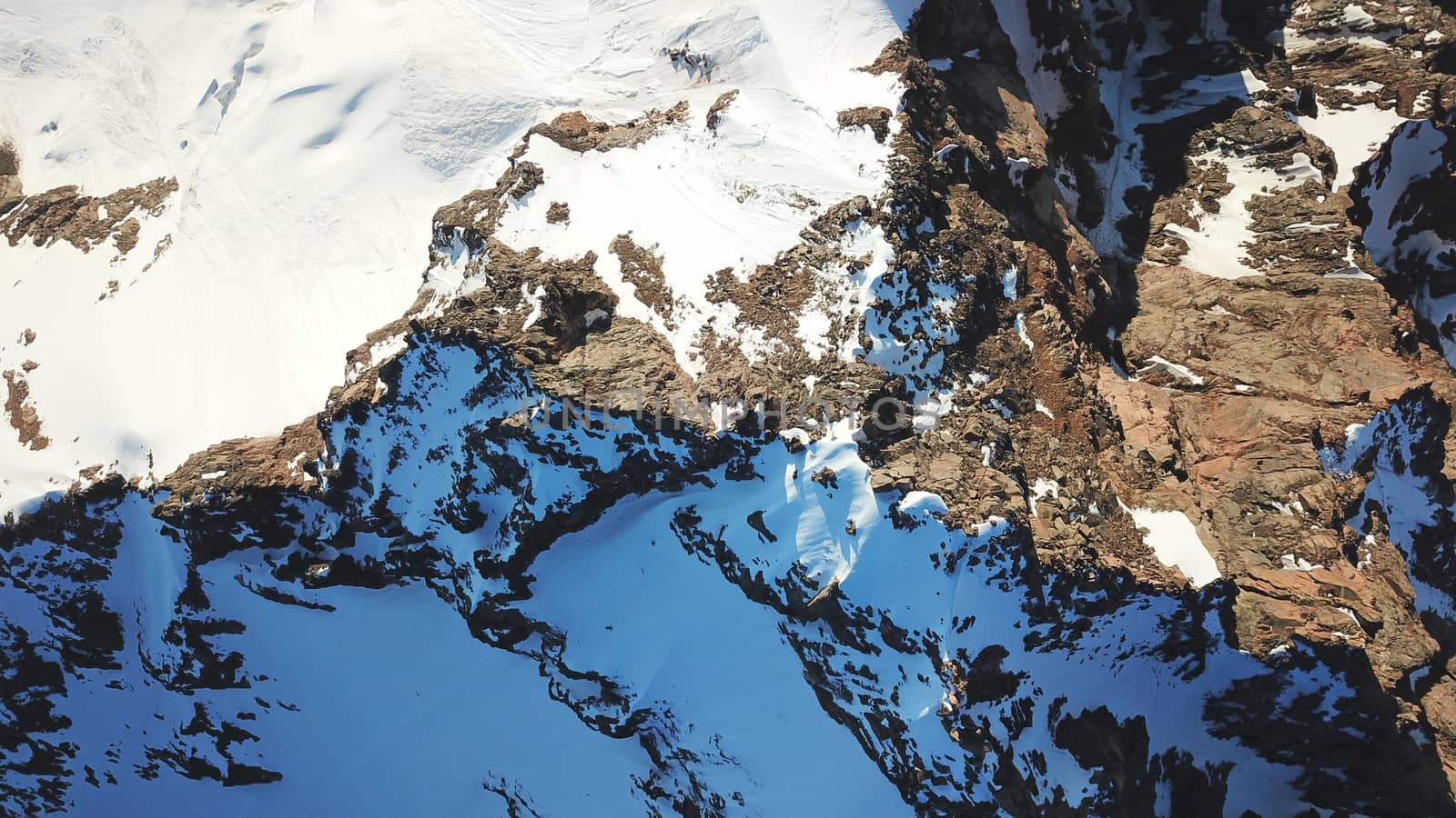 People on the top of a snowy mountain. Top view from a drone. Huge rocks covered with snow, climbers stand on top of the peak. Extreme rest. Steep slopes where there may be an avalanche. Highest peak