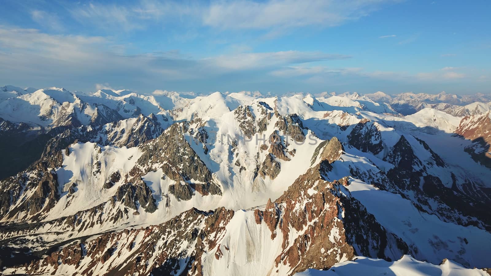 Huge snow mountains. View from the top of the drone. In places, you can see small people climbing to the top. Panorama of steep peaks and rocks, snow cornices. Mountaineering class. Extreme rest.