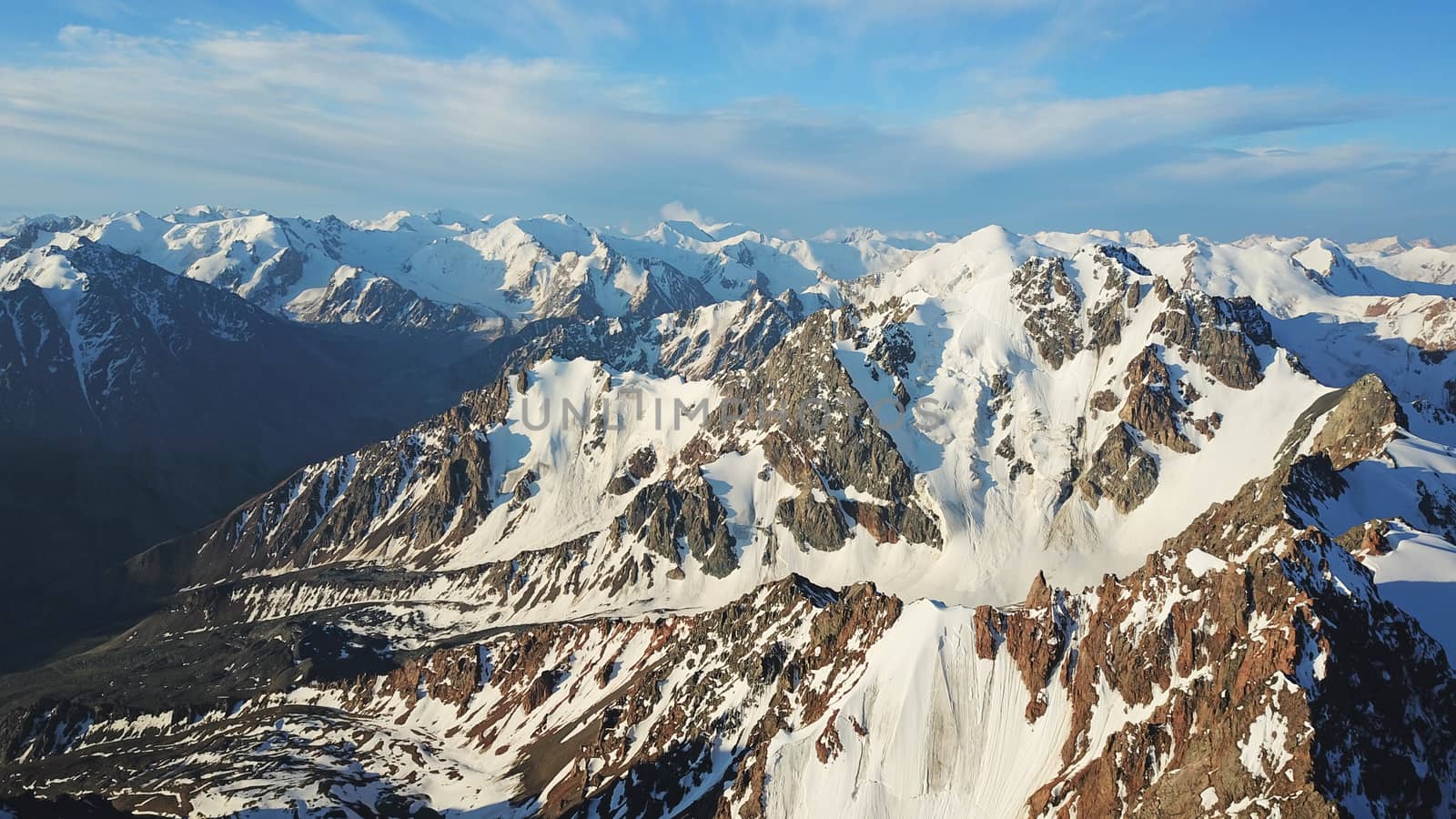 Huge snow mountains. View from the top of the drone. In places, you can see small people climbing to the top. Panorama of steep peaks and rocks, snow cornices. Mountaineering class. Extreme rest.