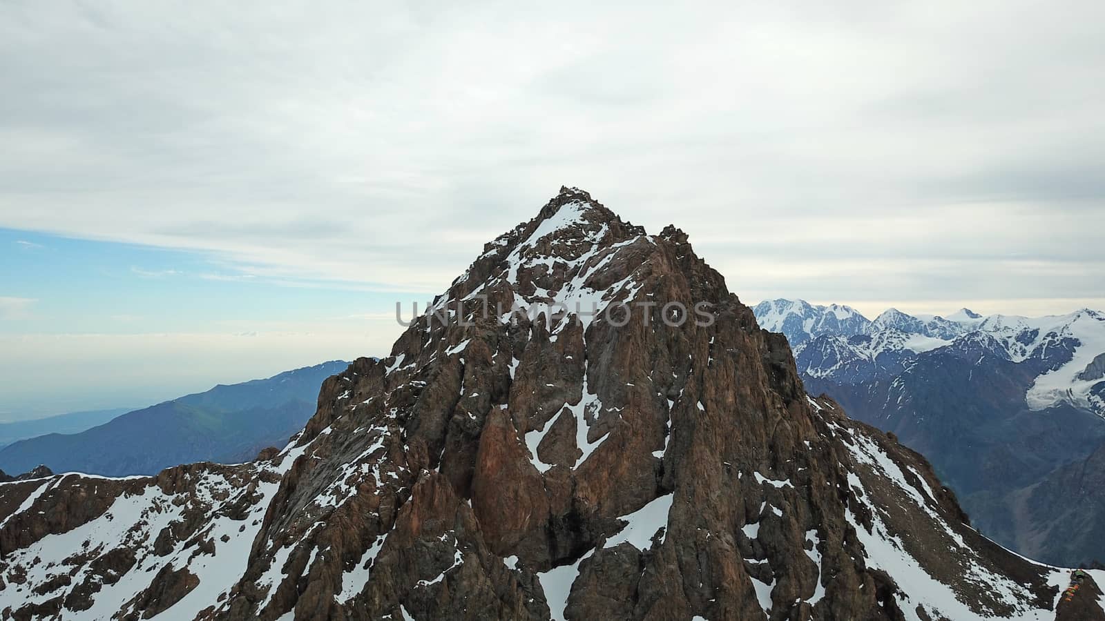 Huge snow mountains. View from the top of the drone. In places, you can see small people climbing to the top. Panorama of steep peaks and rocks, snow cornices. Mountaineering class. Extreme rest.