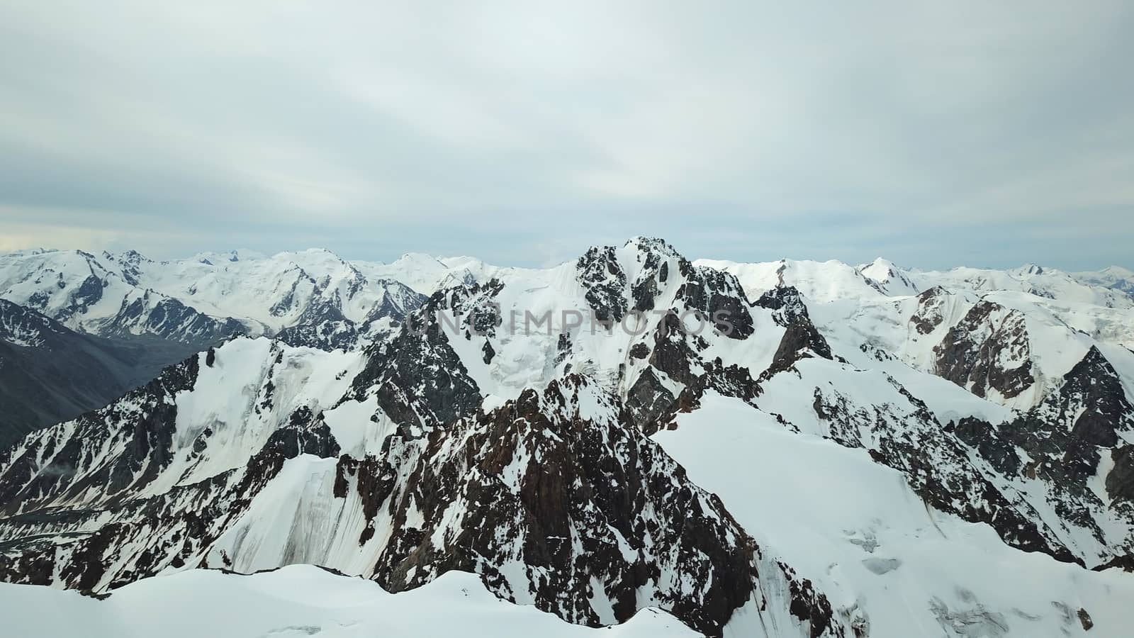 Huge snow mountains. View from the top of the drone. In places, you can see small people climbing to the top. Panorama of steep peaks and rocks, snow cornices. Mountaineering class. Extreme rest.