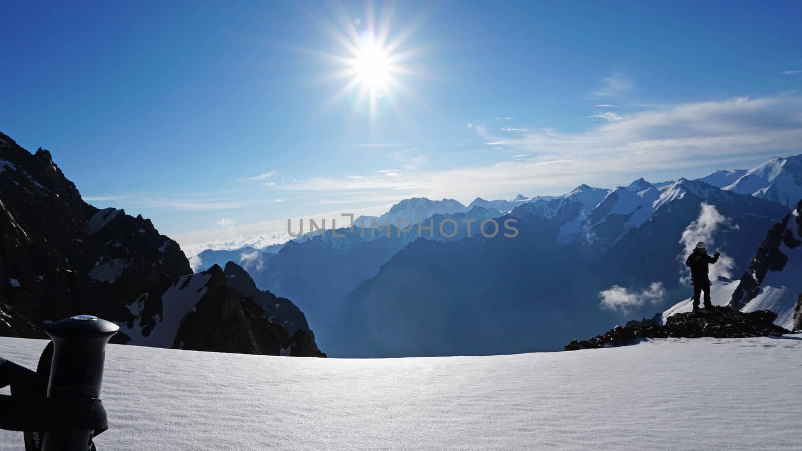 Trekking sticks on the background of snow peaks. The sun is shining brightly, white clouds and snow cliffs in the distance. Blue clear sky. Climbers are going to the top. Alpine camp in the mountains.