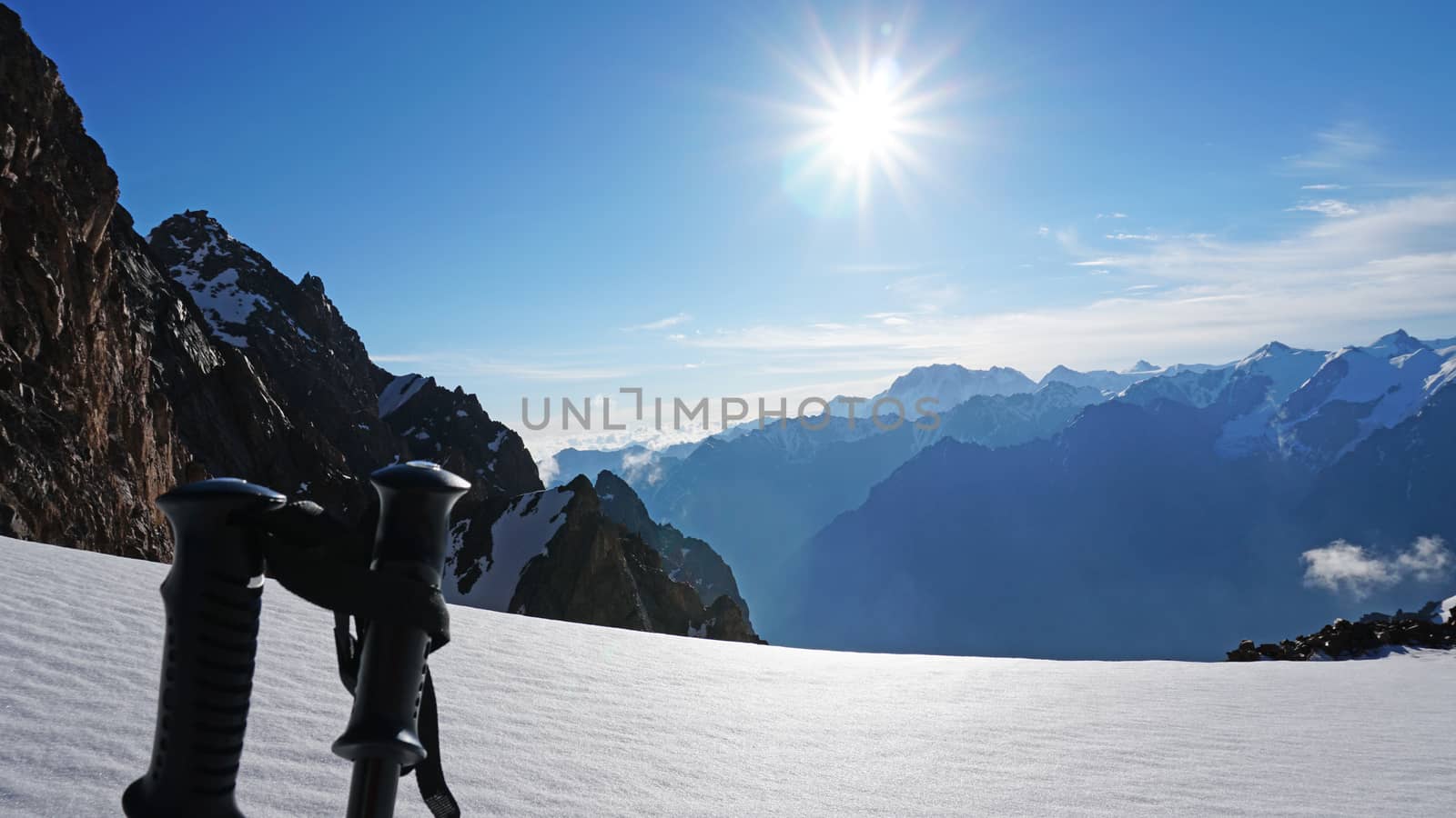 Trekking sticks on the background of snow peaks. The sun is shining brightly, white clouds and snow cliffs in the distance. Blue clear sky. Climbers are going to the top. Alpine camp in the mountains.