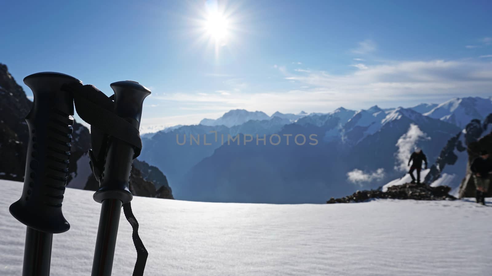 Trekking sticks on the background of snow peaks. The sun is shining brightly, white clouds and snow cliffs in the distance. Blue clear sky. Climbers are going to the top. Alpine camp in the mountains.