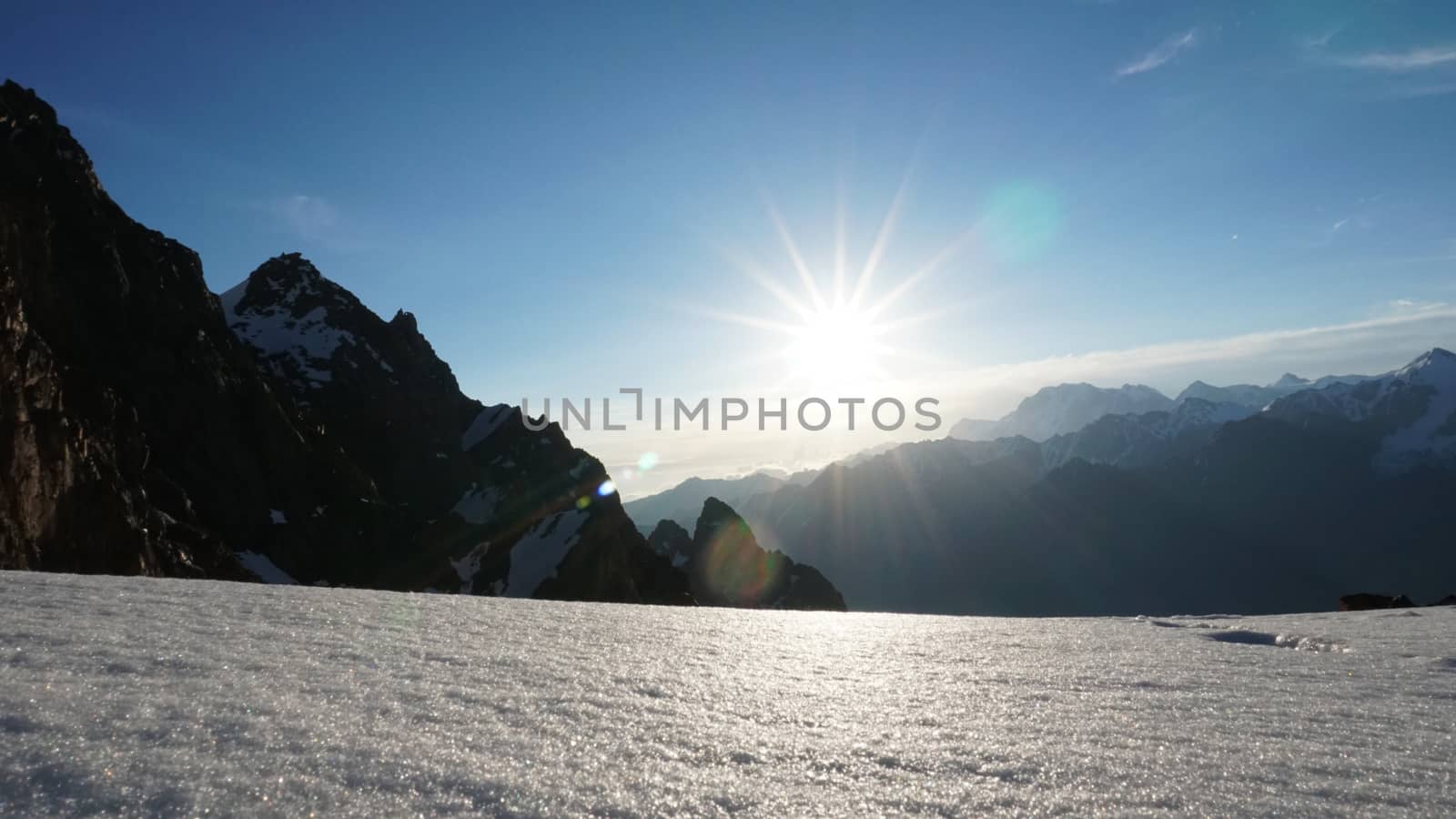 Dawn in the snow-capped mountains. View of the bright sun, mountains and rocks, snow cornice. Snowflakes fly, clouds float. The height is more than 4000 meters. TRANS-Ili Alatau, Kazhastan.