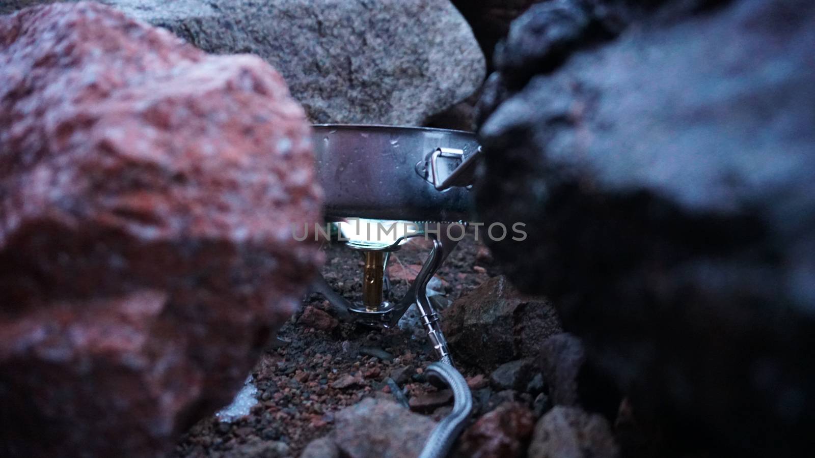 The process of cooking on the burner. Portable stove among the stones. The fire is already burning. Powered by gas. The snow is melting. A convenient device for Hiking and a small pot. Journey.