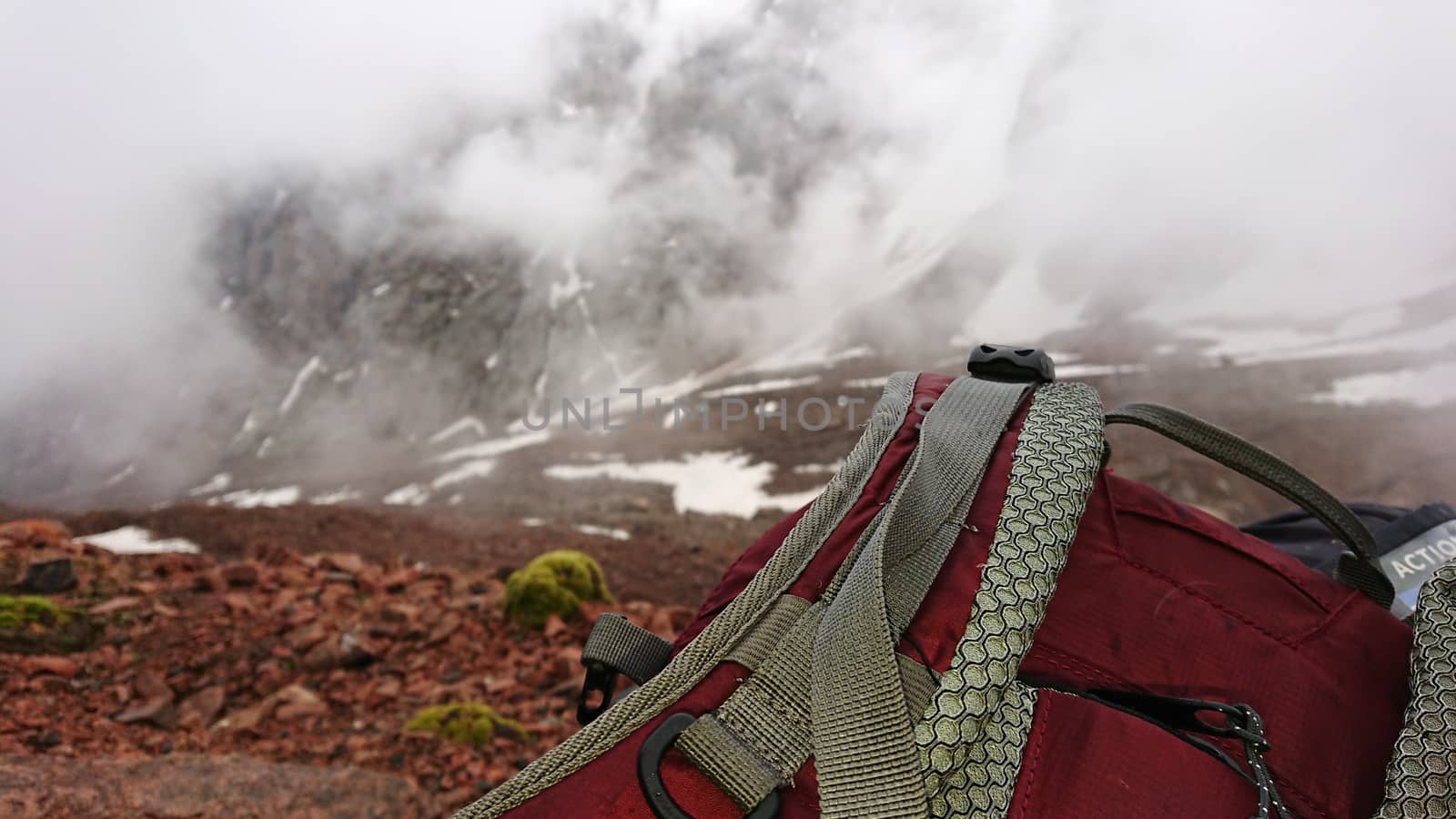 Backpack in the snowy mountains. Fog is coming. An Alpine camp in the rocky mountains, sometimes there is snow. Big clouds are passing. Mountain tops in the clouds. The ascent to the peak.