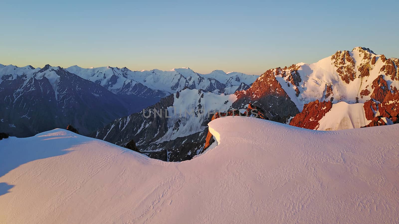 Epic red dawn on top of snowy mountains. Top view from a drone. Huge rocks covered with snow, the ledge of snow overhangs. An avalanche-prone place. Climb to the peak. Flying above the peak. Almaty