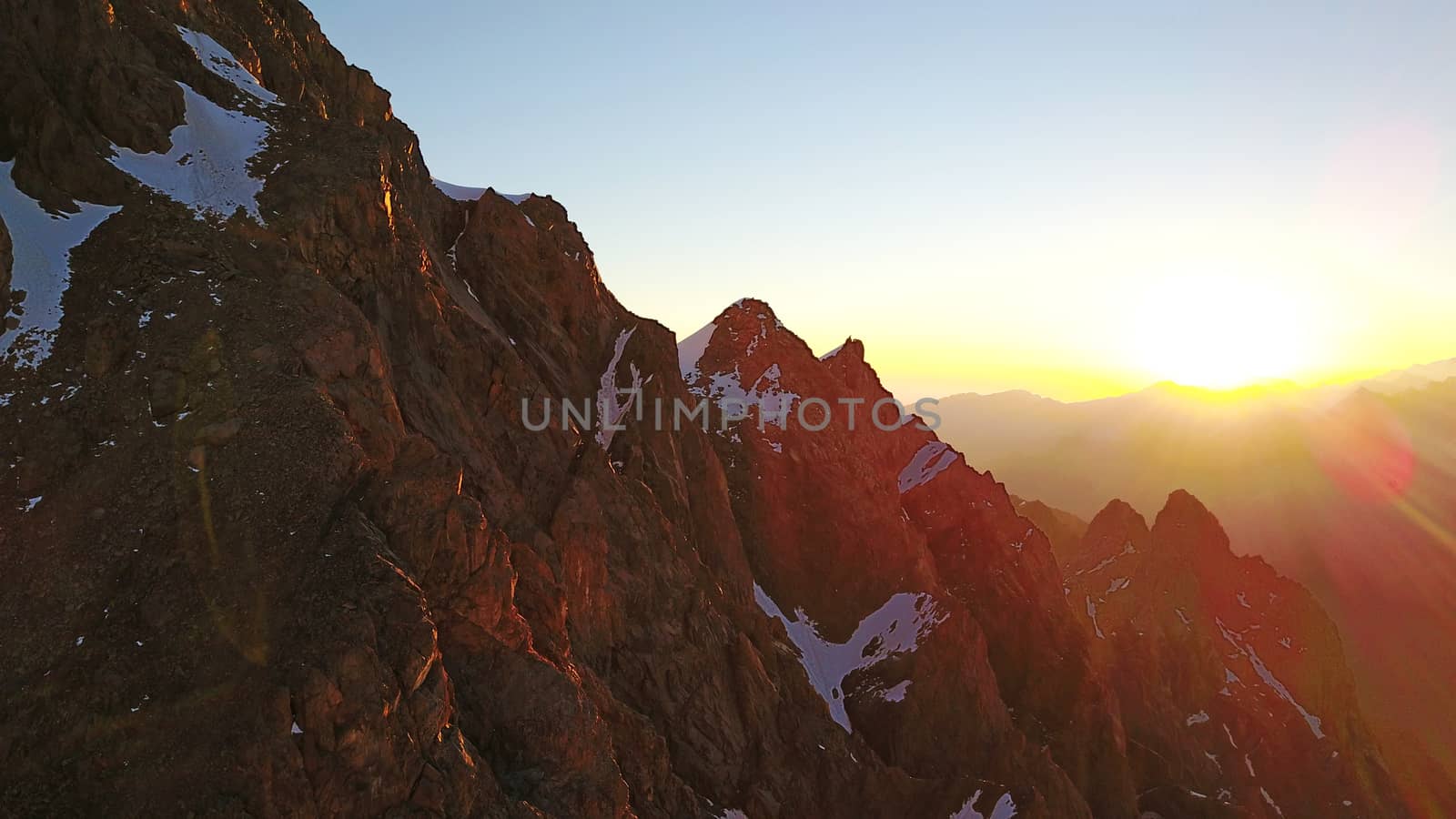 Epic red dawn on top of snowy mountains. Top view from a drone. Huge rocks covered with snow, the ledge of snow overhangs. An avalanche-prone place. Climb to the peak. Flying above the peak. Almaty