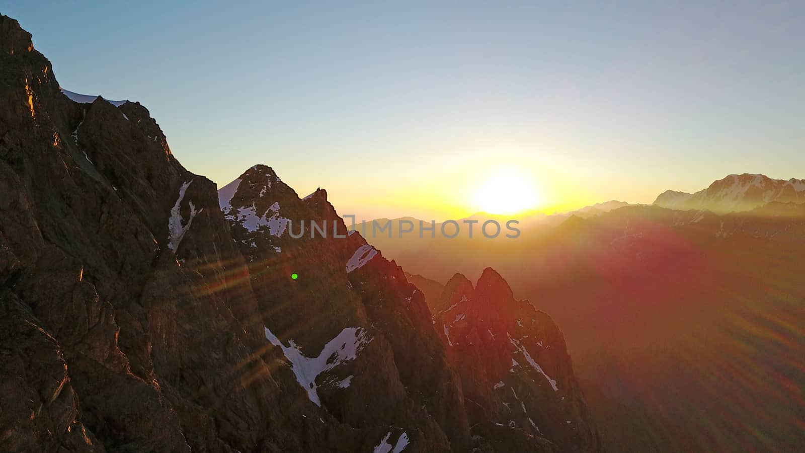 Epic red dawn on top of snowy mountains. Top view from a drone. Huge rocks covered with snow, the ledge of snow overhangs. An avalanche-prone place. Climb to the peak. Flying above the peak. Almaty