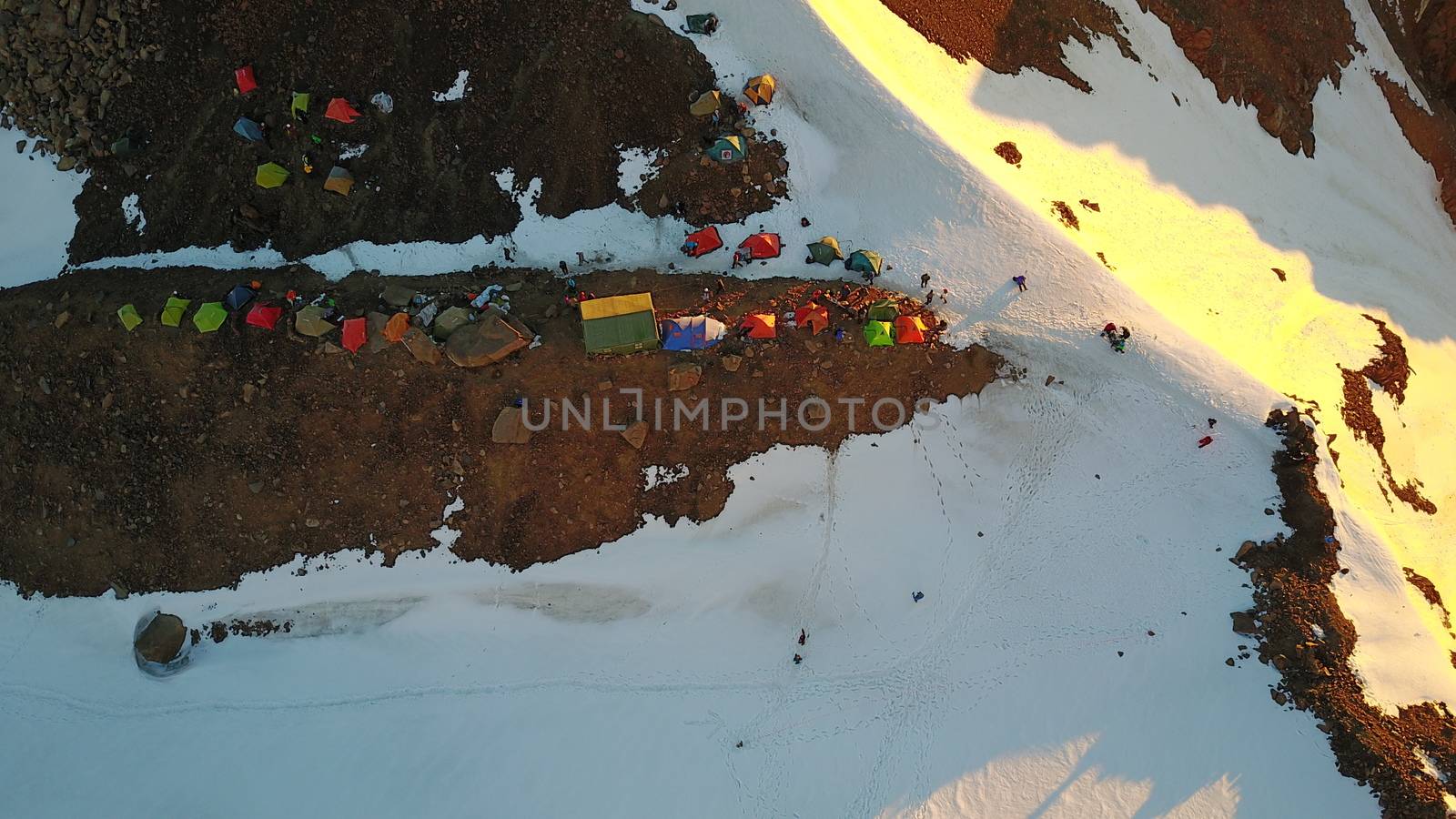 Mountaineering camp high in the snowy mountains. Epic red dawn, top view from a drone. Camp on the edge of the cliff. The snow-capped peaks, huge rocks. Preparing to climb the peak. Lots of tents.