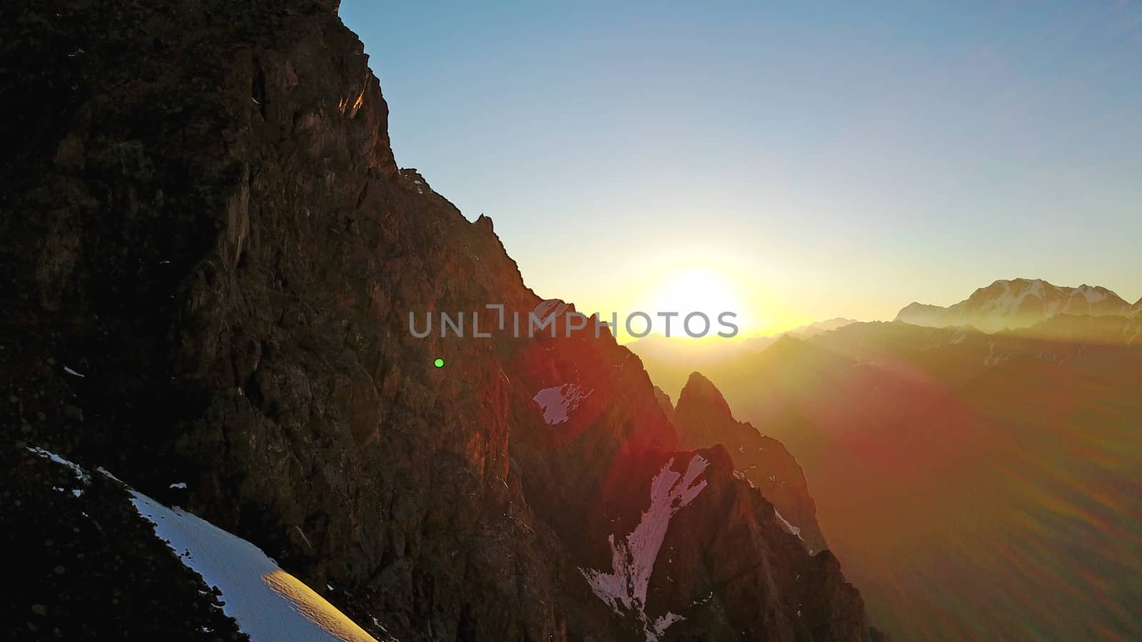 Epic red dawn on top of snowy mountains. Top view from a drone. Huge rocks covered with snow, the ledge of snow overhangs. An avalanche-prone place. Climb to the peak. Flying above the peak. Almaty