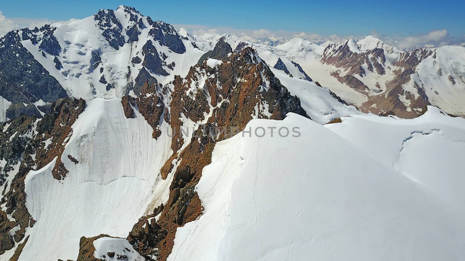 Huge snow mountains. View from the top of the drone. In places, you can see small people climbing to the top. Panorama of steep peaks and rocks, snow cornices. Mountaineering class. Extreme rest.