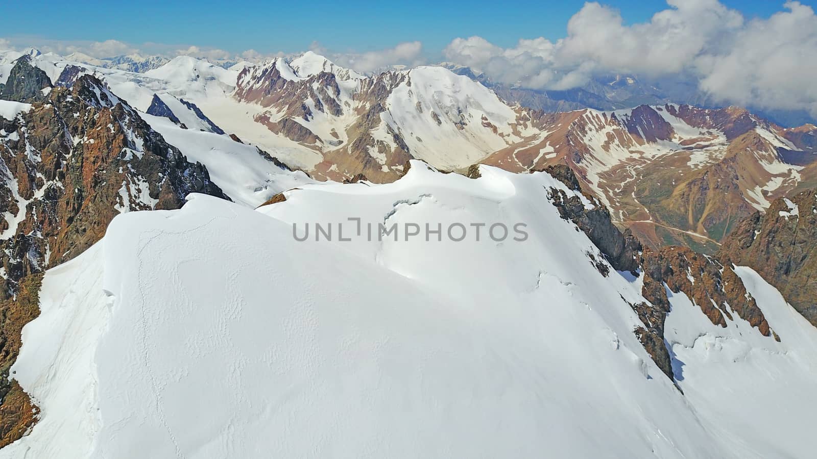 Huge snow mountains. View from the top of the drone. In places, you can see small people climbing to the top. Panorama of steep peaks and rocks, snow cornices. Mountaineering class. Extreme rest.