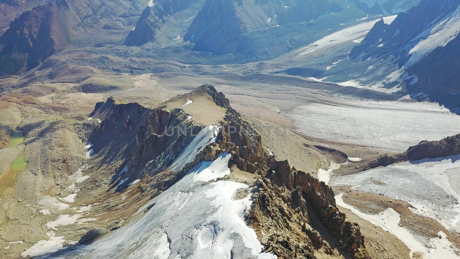 Huge snow mountains. View from the top of the drone. In places, you can see small people climbing to the top. Panorama of steep peaks and rocks, snow cornices. Mountaineering class. Extreme rest.