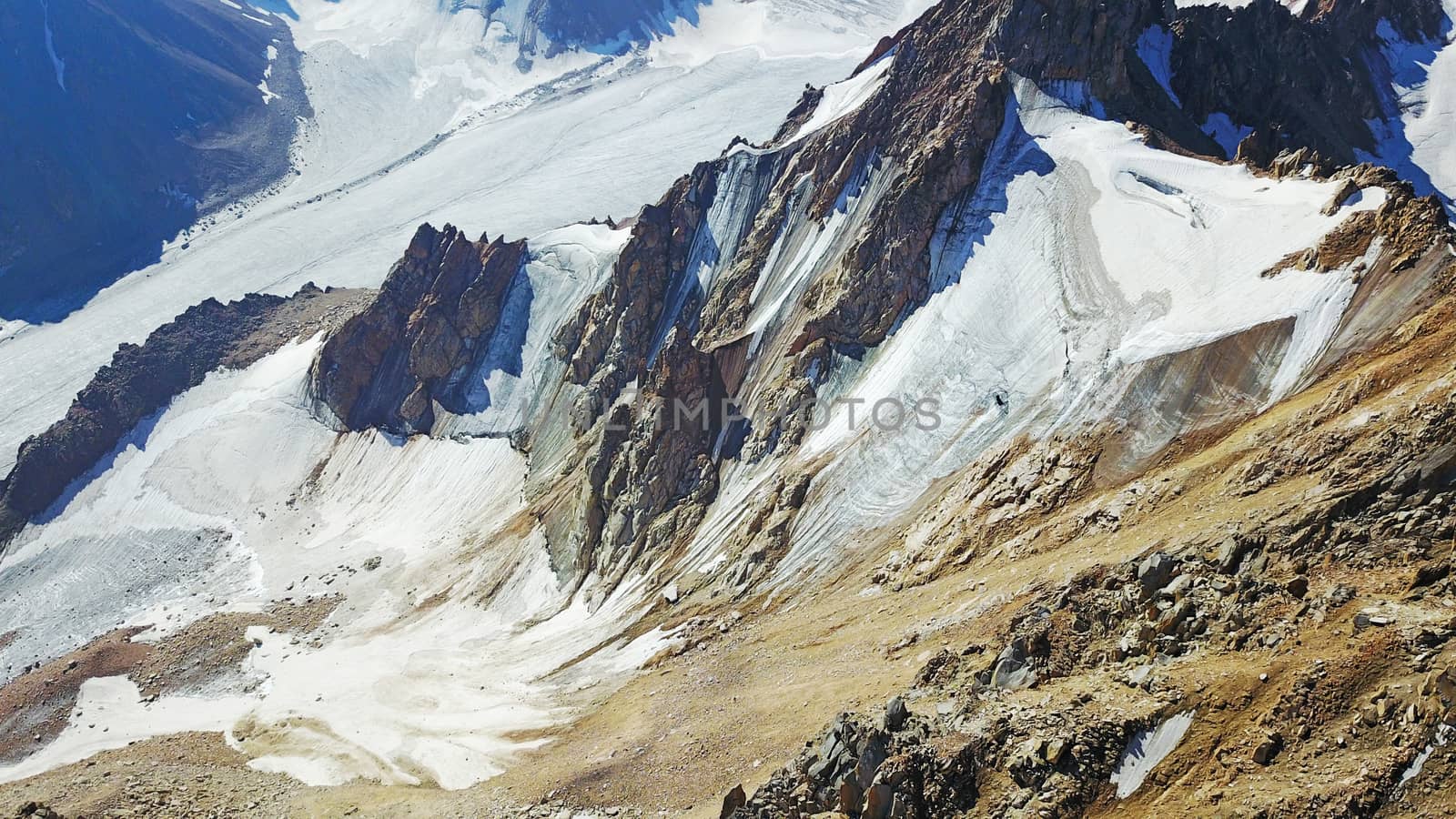 Huge snow mountains. View from the top of the drone. In places, you can see small people climbing to the top. Panorama of steep peaks and rocks, snow cornices. Mountaineering class. Extreme rest.