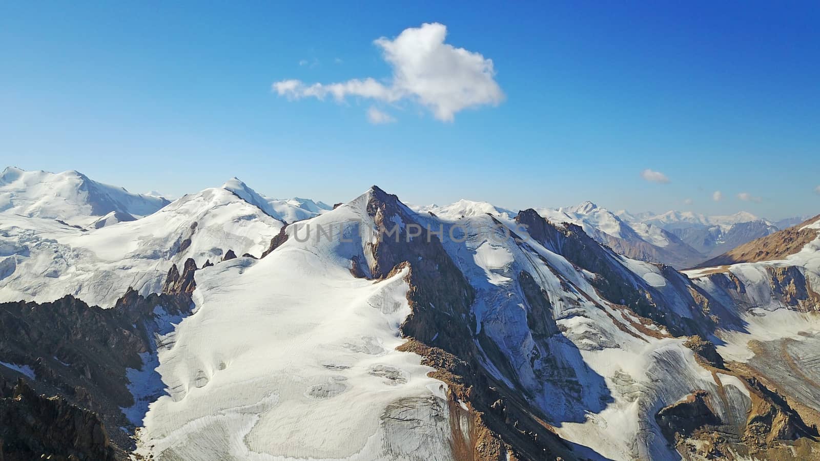 Huge snow mountains. View from the top of the drone. In places, you can see small people climbing to the top. Panorama of steep peaks and rocks, snow cornices. Mountaineering class. Extreme rest.