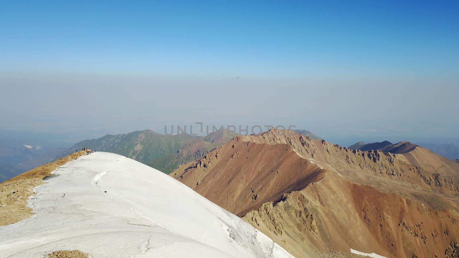 Huge snow mountains. View from the top of the drone. In places, you can see small people climbing to the top. Panorama of steep peaks and rocks, snow cornices. Mountaineering class. Extreme rest.